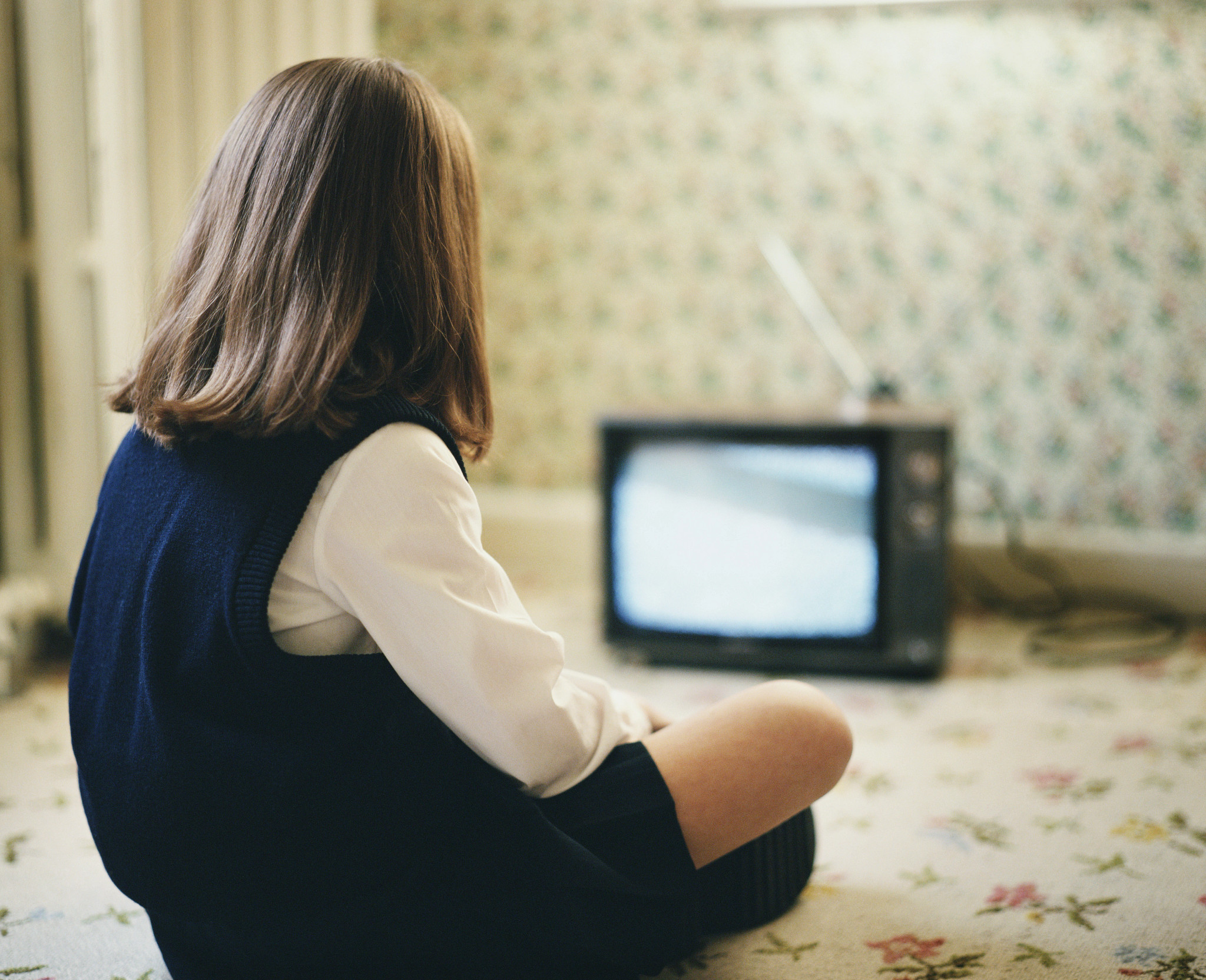 a photo shows a young girl watching a TV with rabbit ears