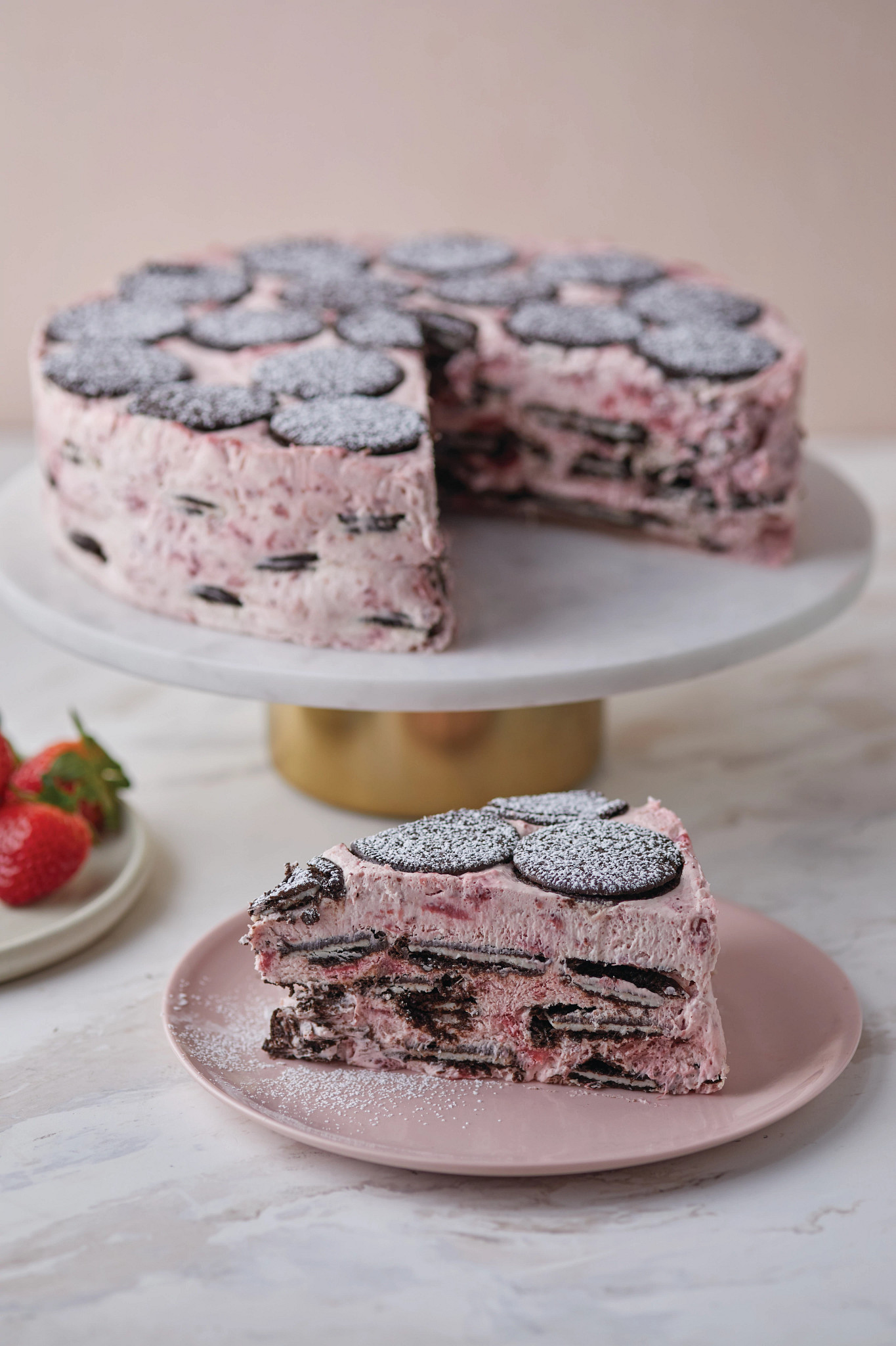 an extreme close-up view of a pink strawberry cake with chocolate cookies on a white cake stand