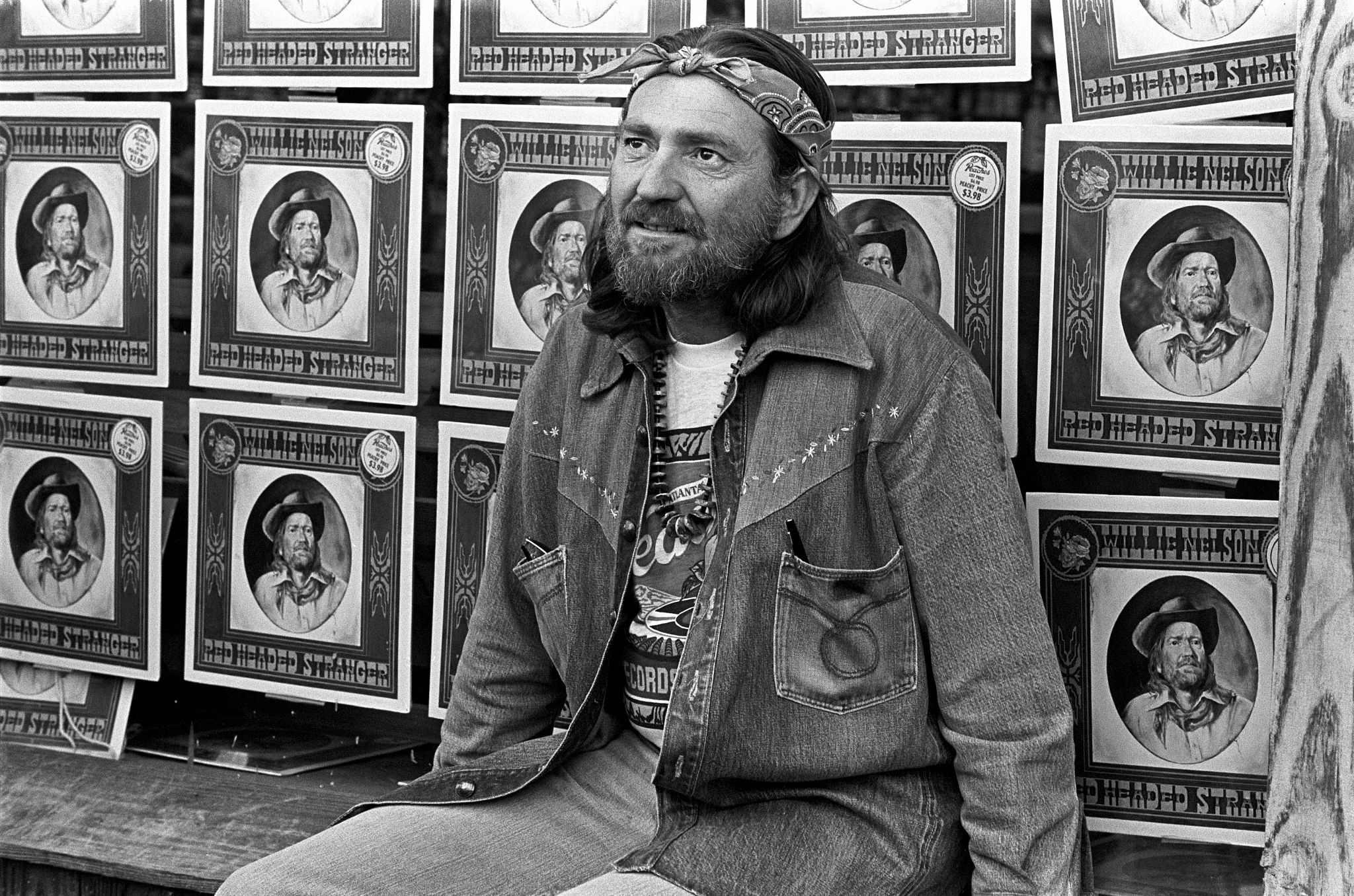 Willie Nelson willie nelson sits on a bench in front of dozens of his red headed stranger album covers