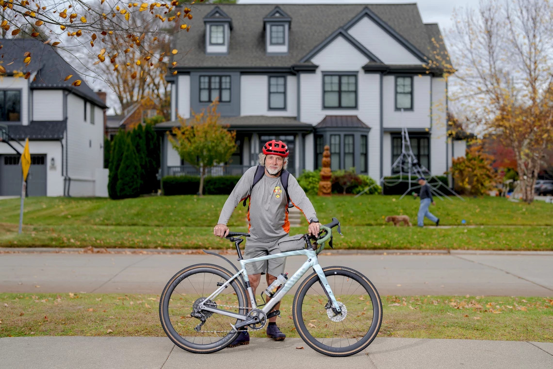 a man, wearing a red helmet, stands with a bicycle on the sidewalk