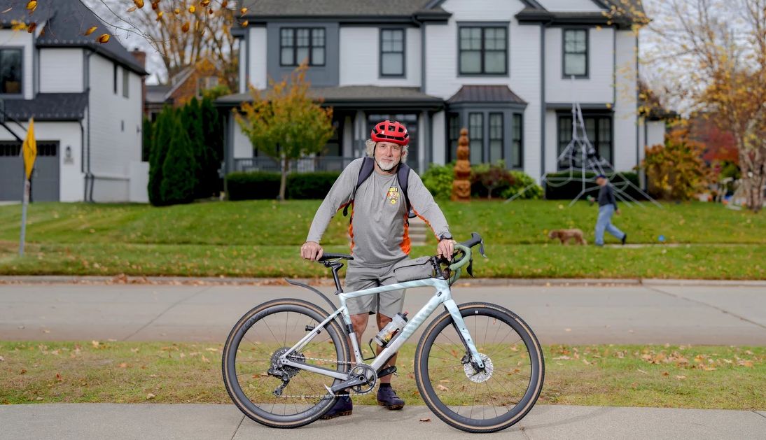 Arthur Stephenson  a man, wearing a red helmet, stands with a bicycle on the sidewalk
