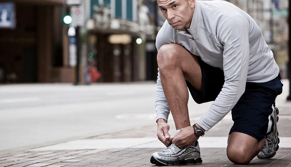 Exercising outside has many health benefits A runner taking a knee to tie his shoe