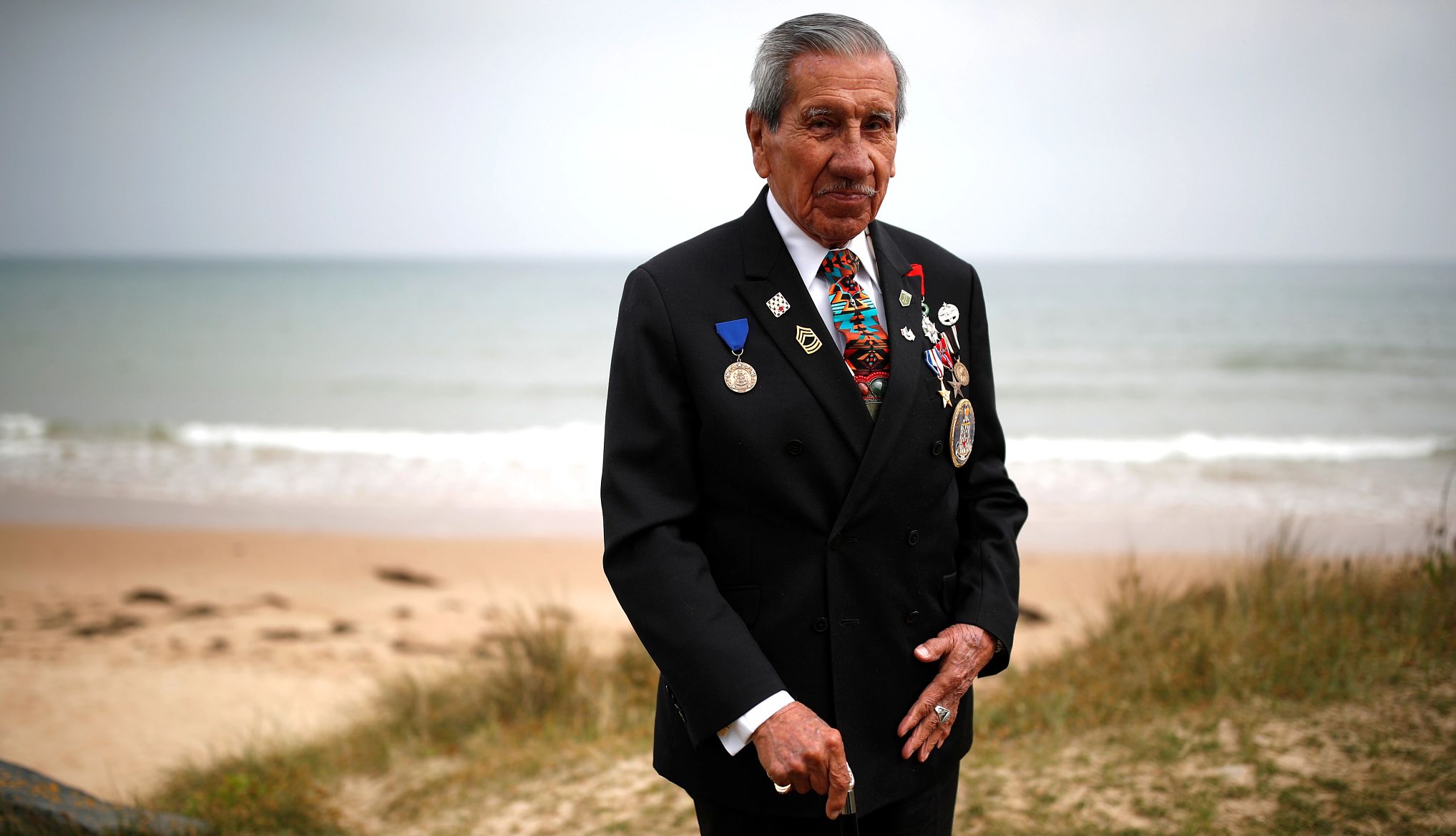 Thank a veteran for the 80th D-Day anniversary Charles Norman Shay stands on a beach in a black suit with multiple military medals pinned to his jacket