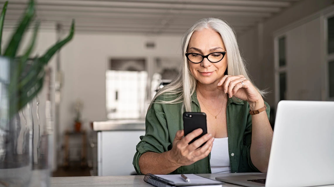 woman with phone & laptop working from home