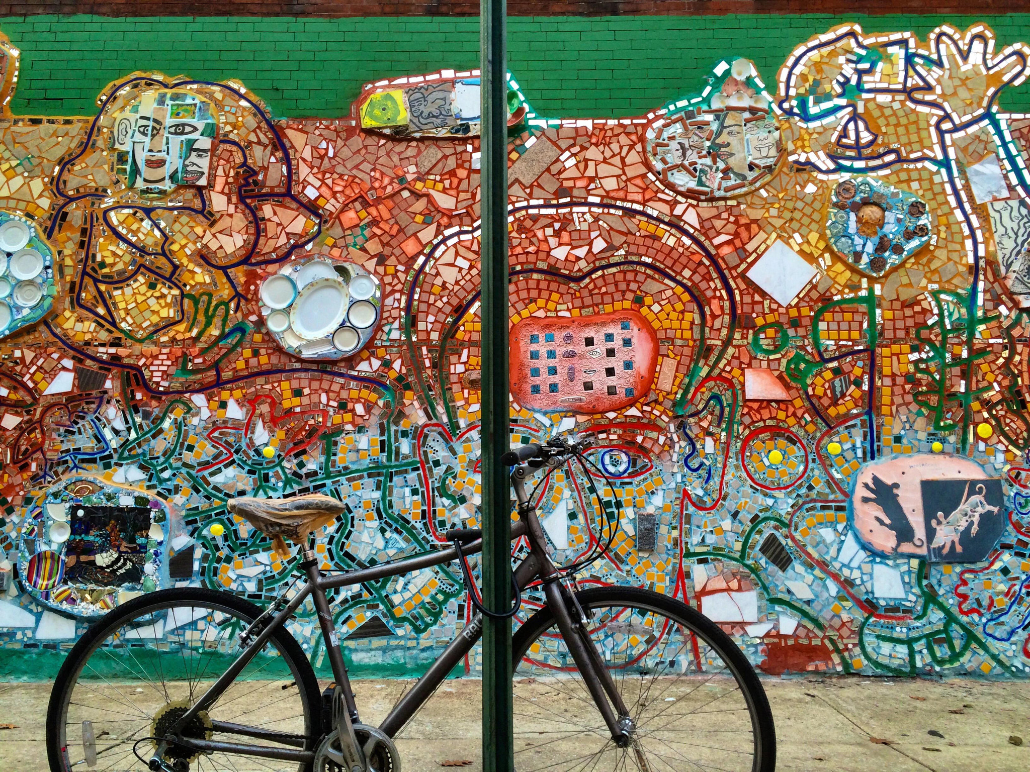 A bicycle parked in front of a vibrant mosaic mural made of colorful ceramic tiles and abstract designs.