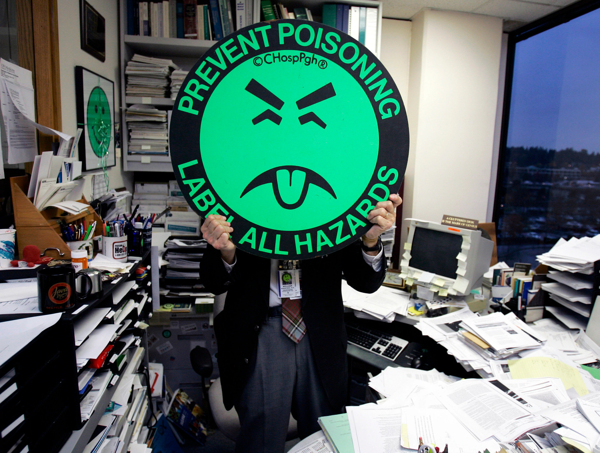 A photo shows a man in an office holding a sign of Mr. Yuk in front of his face