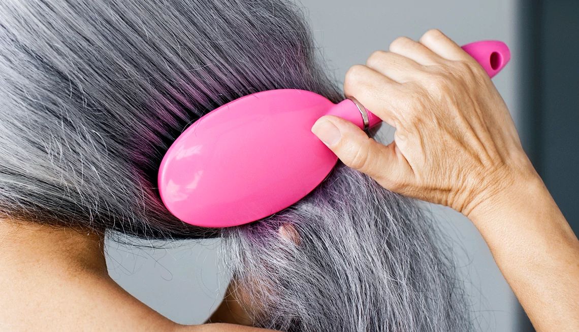 close up of a woman brushing long gray hair with a purple hair brush