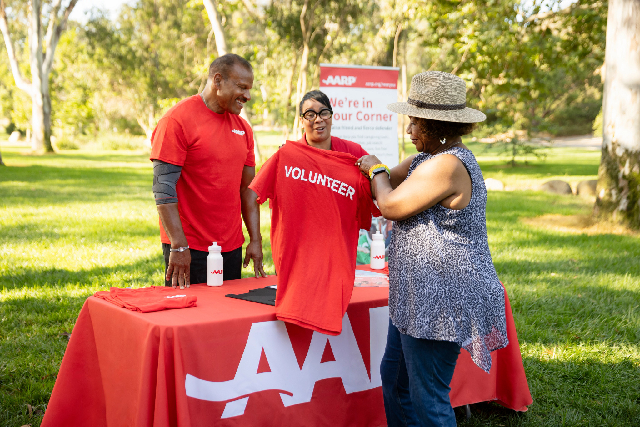A A R P volunteers sharing a volunteer T-shirt at an outdoor event booth