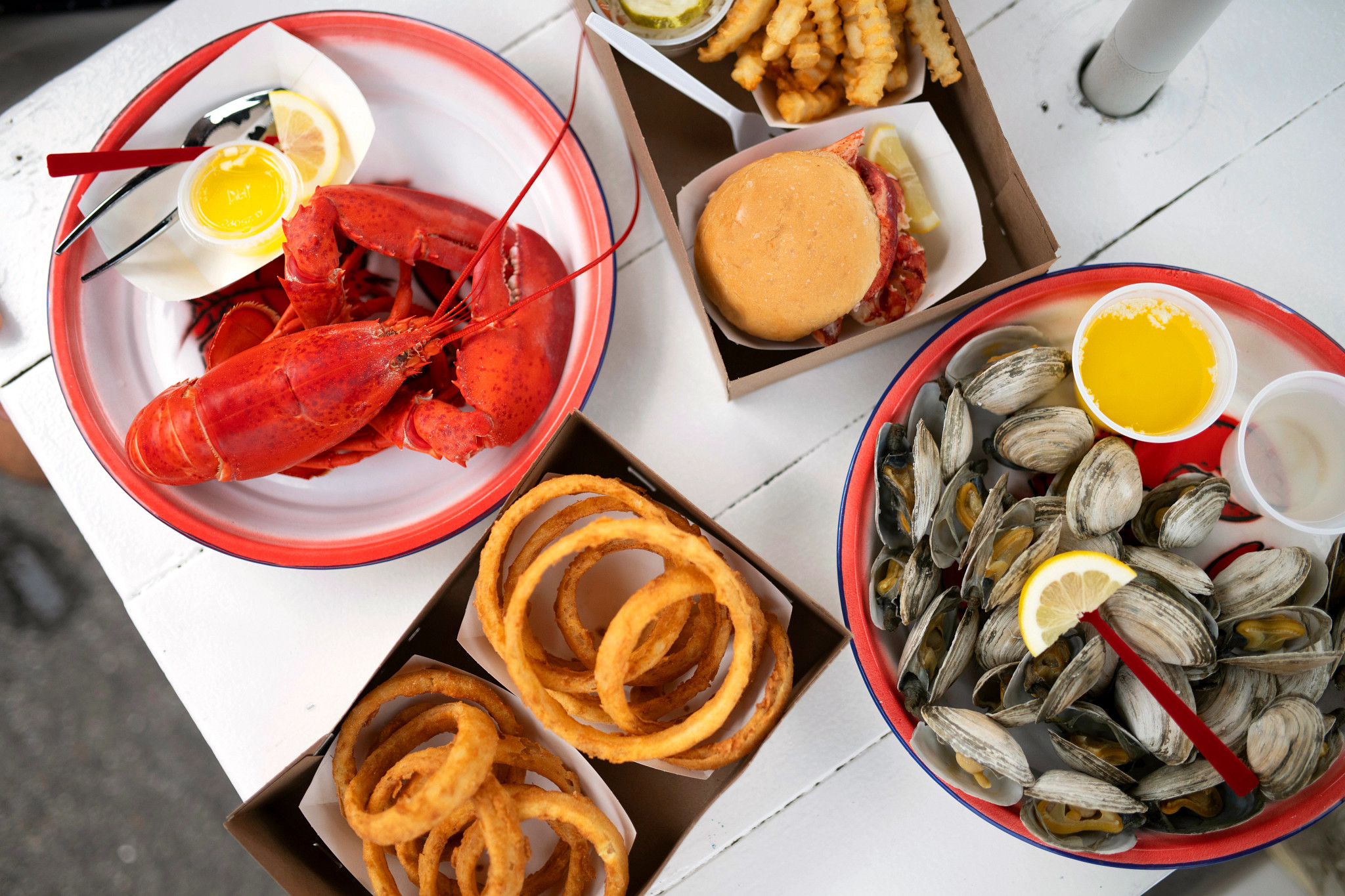 a closeup shot of lobster, onion rings, a burger and clams