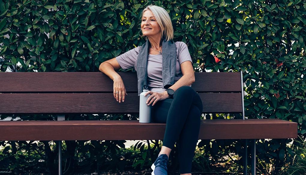 Keeping a water bottle always nearby can help you stay hydrated A woman sitting on a park bench with a water bottle in her hand