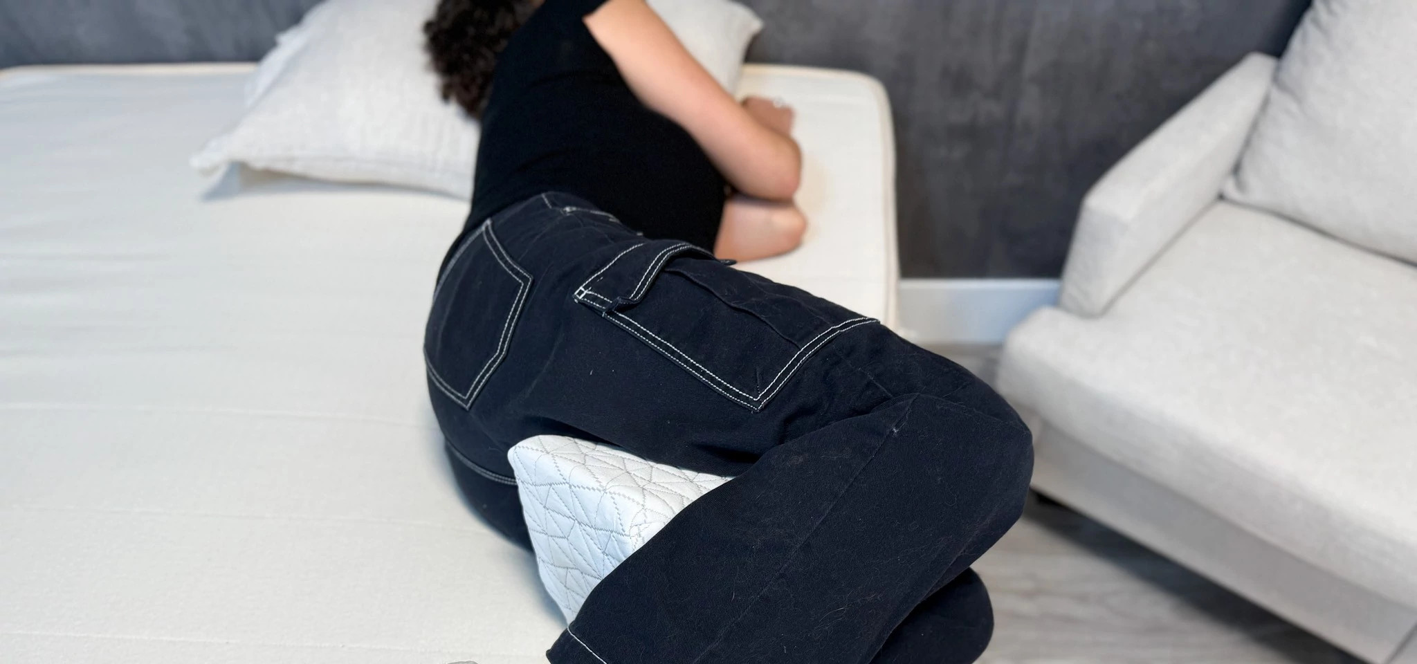 A person lying on their side on a mattress with a Coop Adjustable Knee pillow between their knees