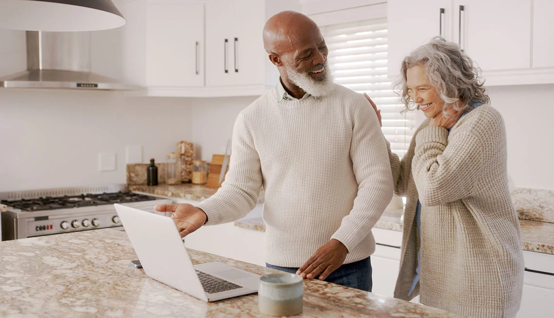 AARP® Medicare Supplement from UnitedHealthcare® man and woman, older, standing at a kitchen island looking at a open laptop, smiling
