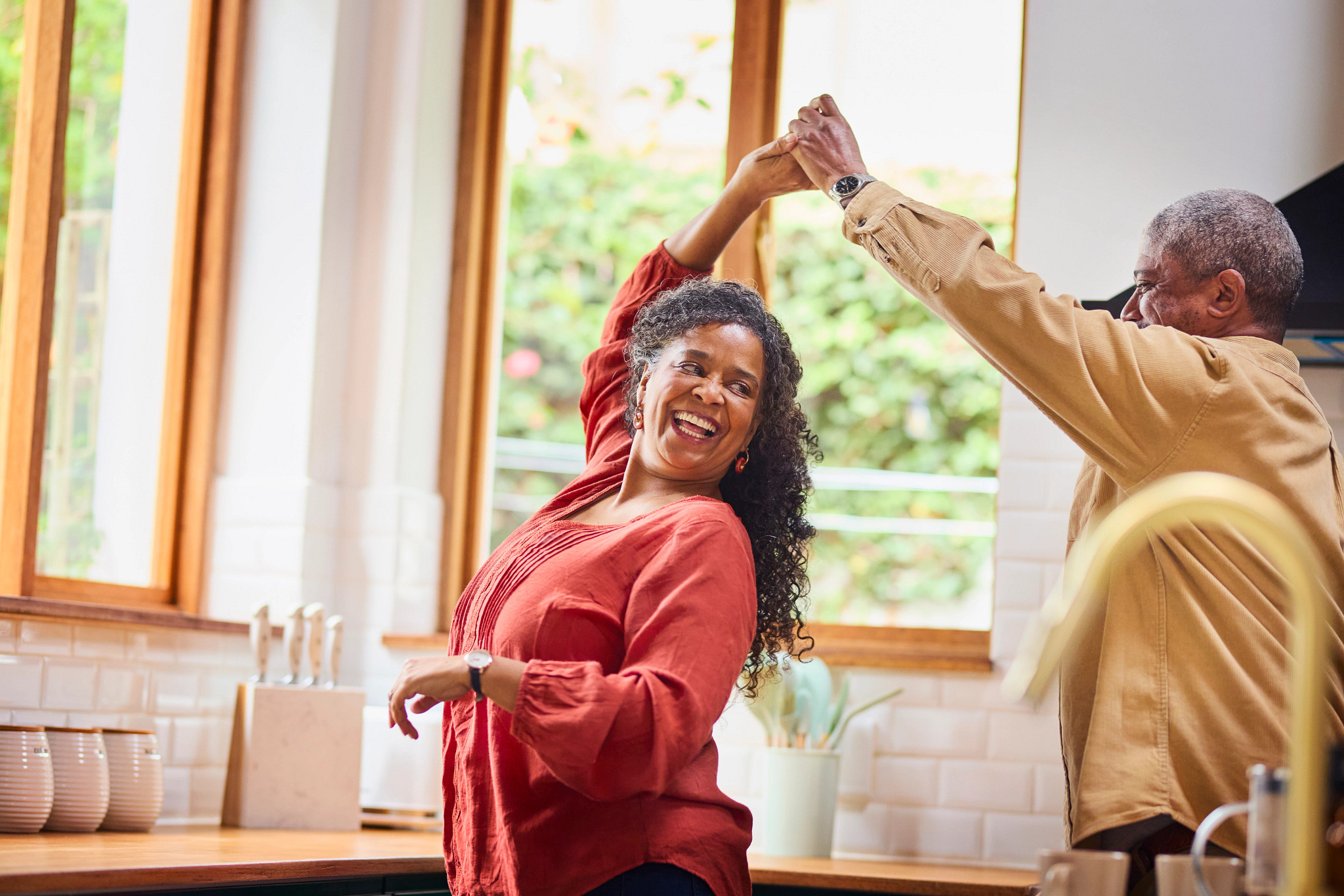 A vibrant senior African American couple joyfully dancing and twirling with hands clasped in their bright, modern kitchen.