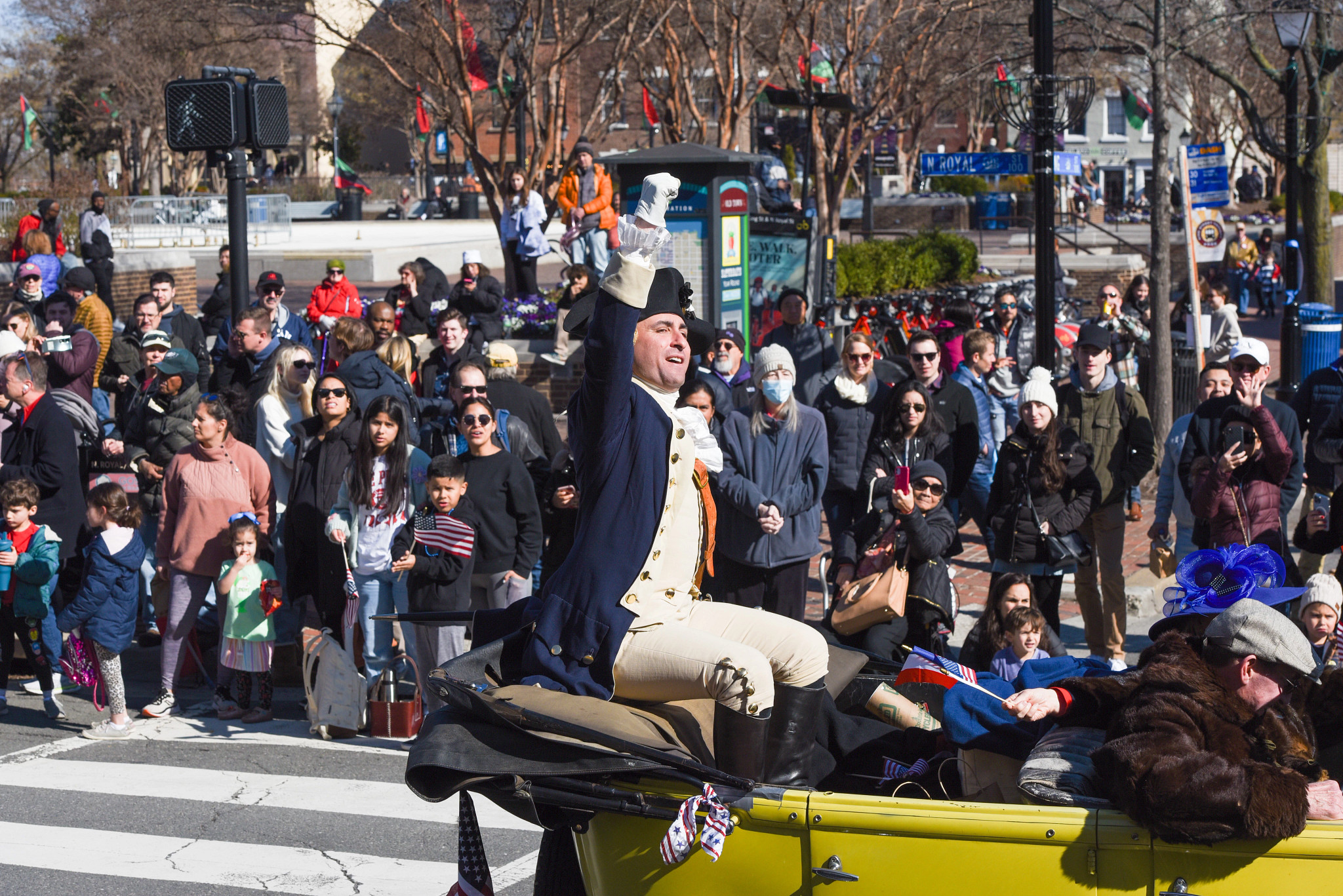 a person dressed as george washington sits in the back of a car during a birthday parade for the president