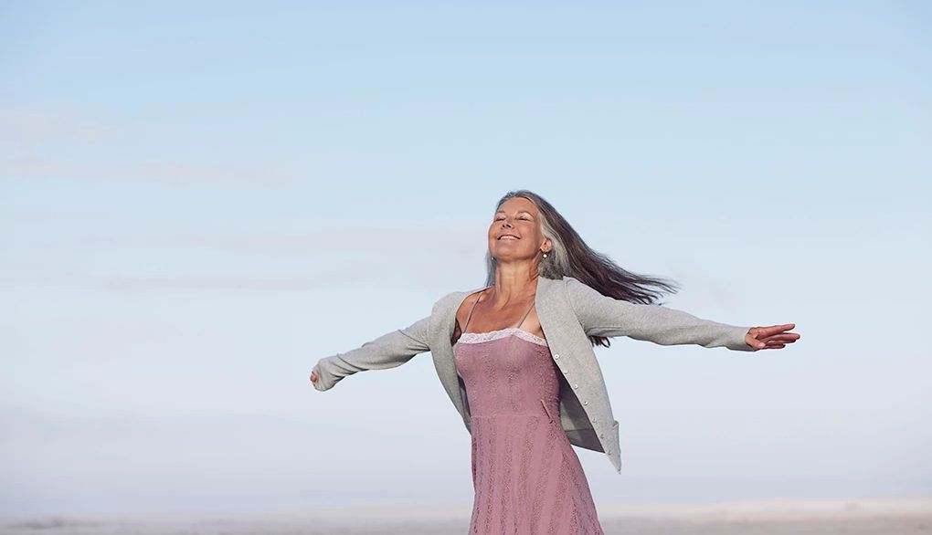 Picture yourself taking the steps to make your goal happen A smiling woman with her arms raised on a beach