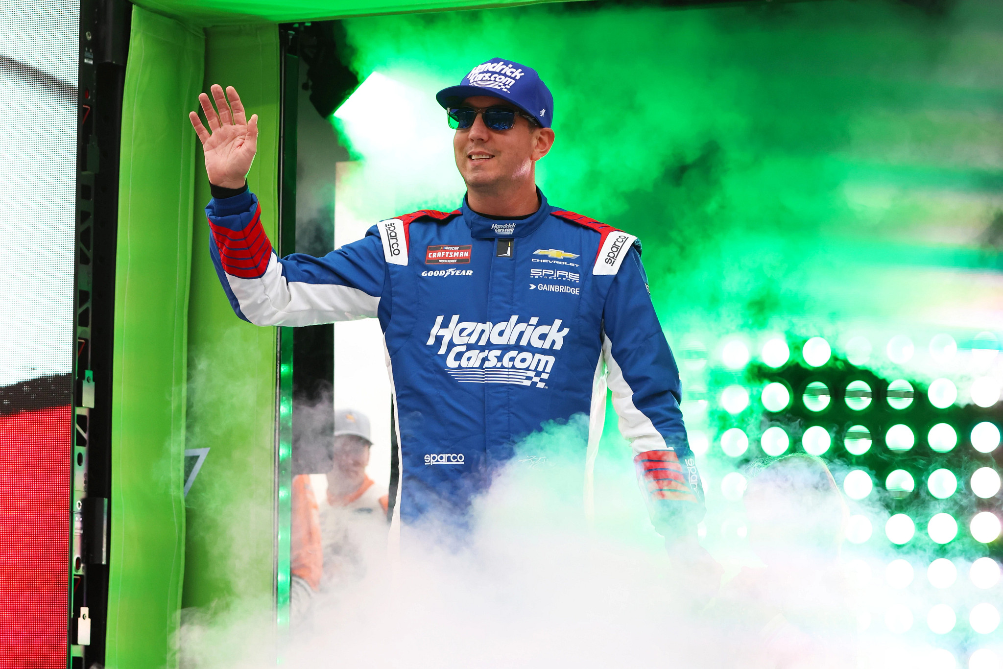 kyle busch waving to crowd in his racing uniform and sunglasses