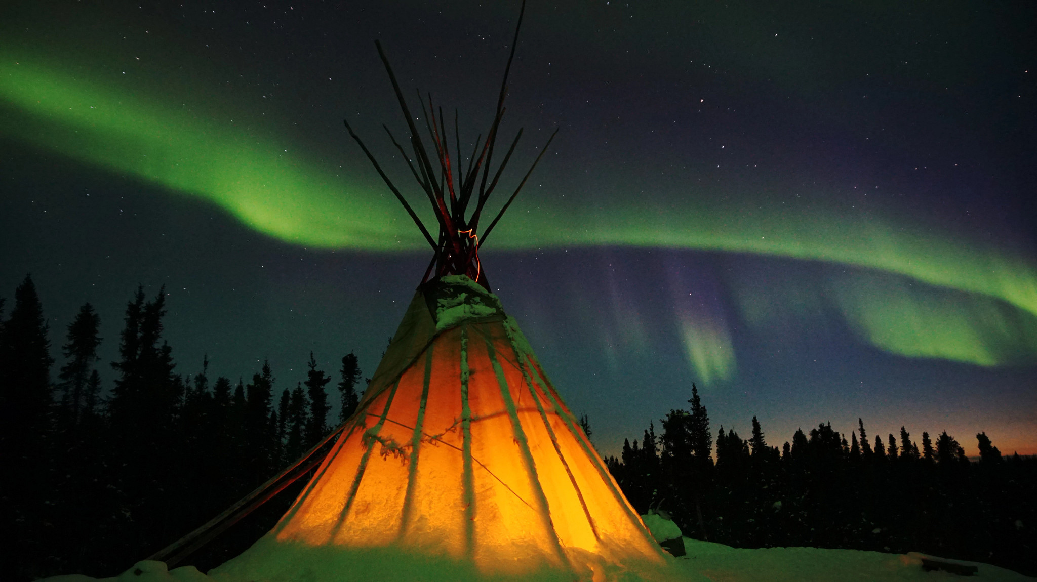 a tepee covered in the snow with the northern lights above
