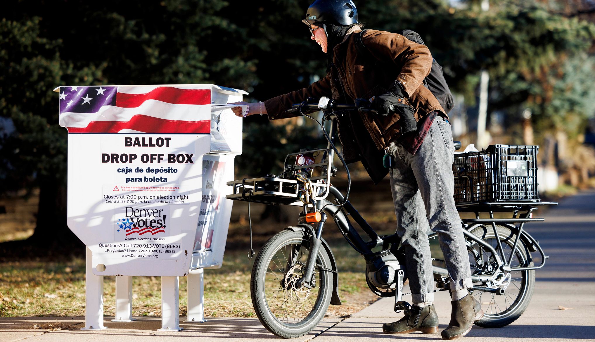 A voter on a bicycle ride drops their ballot into a ballot drop-off box