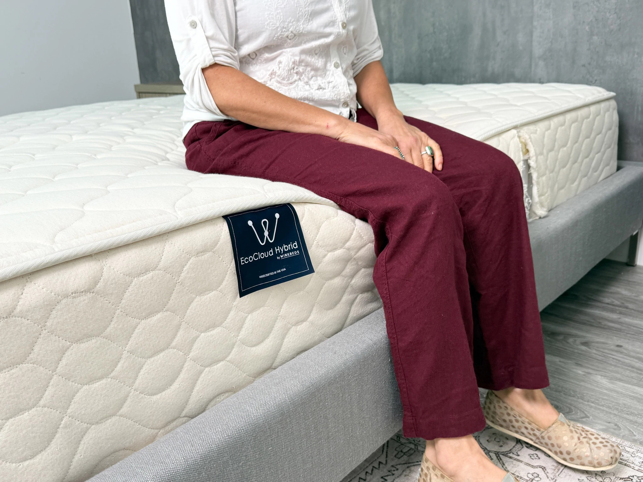 A person sits on the edge of the WinkBeds EcoCloud mattress.