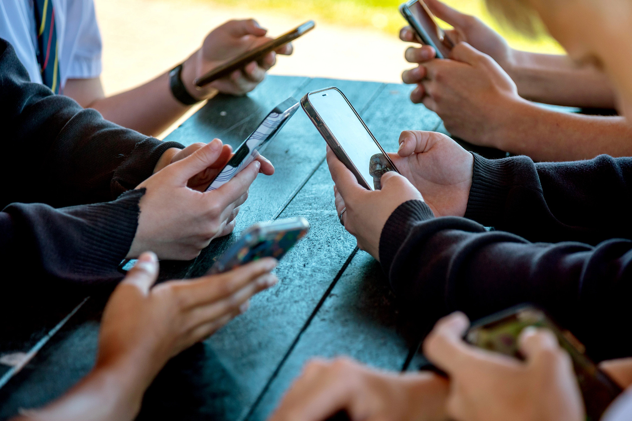 a photo shows teenagers looking at their phone screens displaying various social media apps