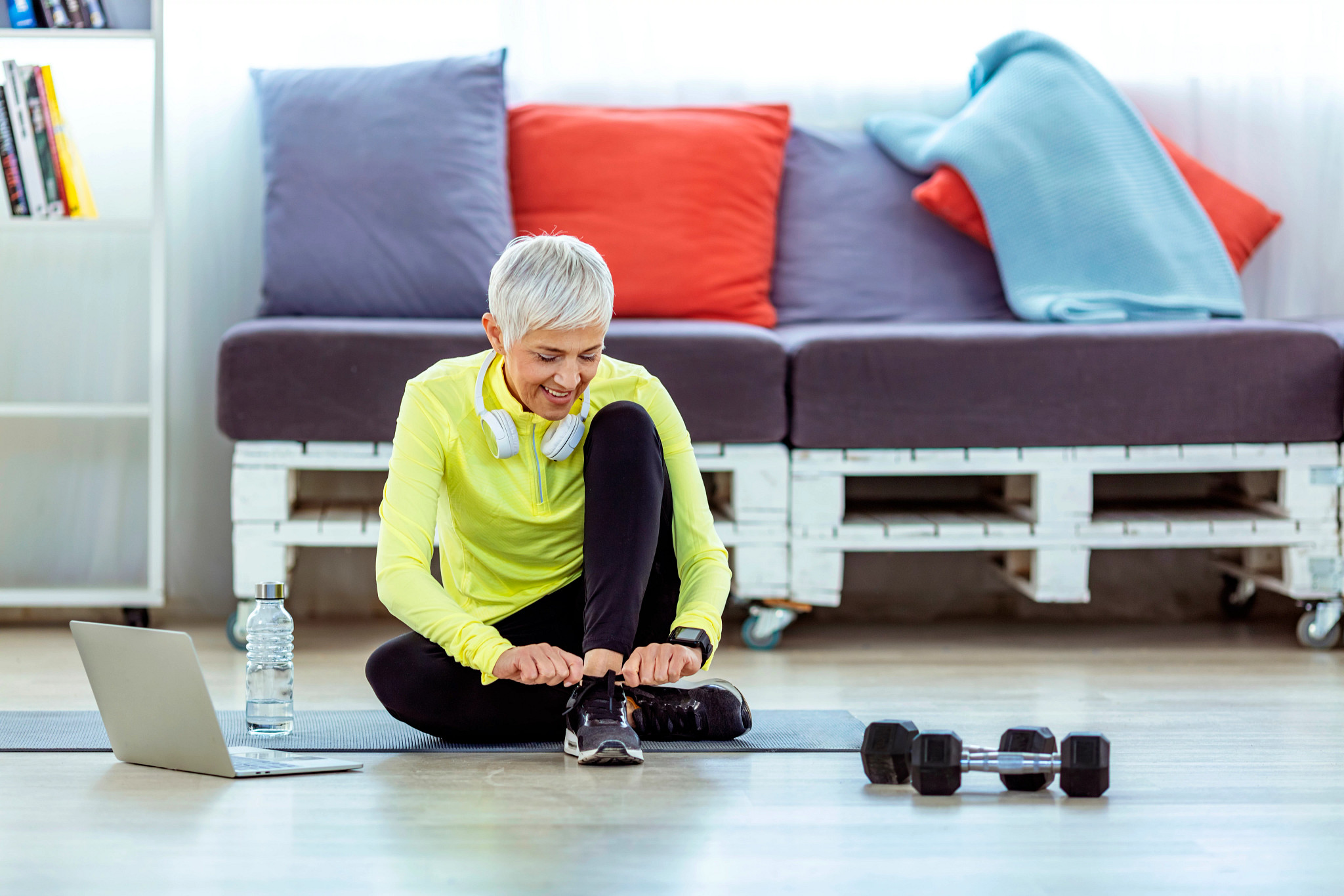 Running shoes - Photo of Mature, gray hair woman tying shoe laces while sitting at home in front of her laptop during the day