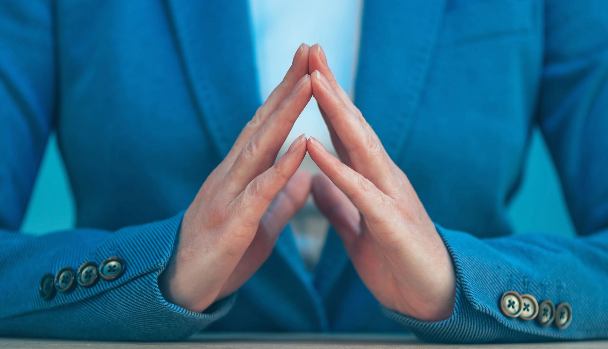 Nonverbal Communication Guide A photo shows a man in a blue suit finger tenting his hands, a way to express confidence nonverbally.