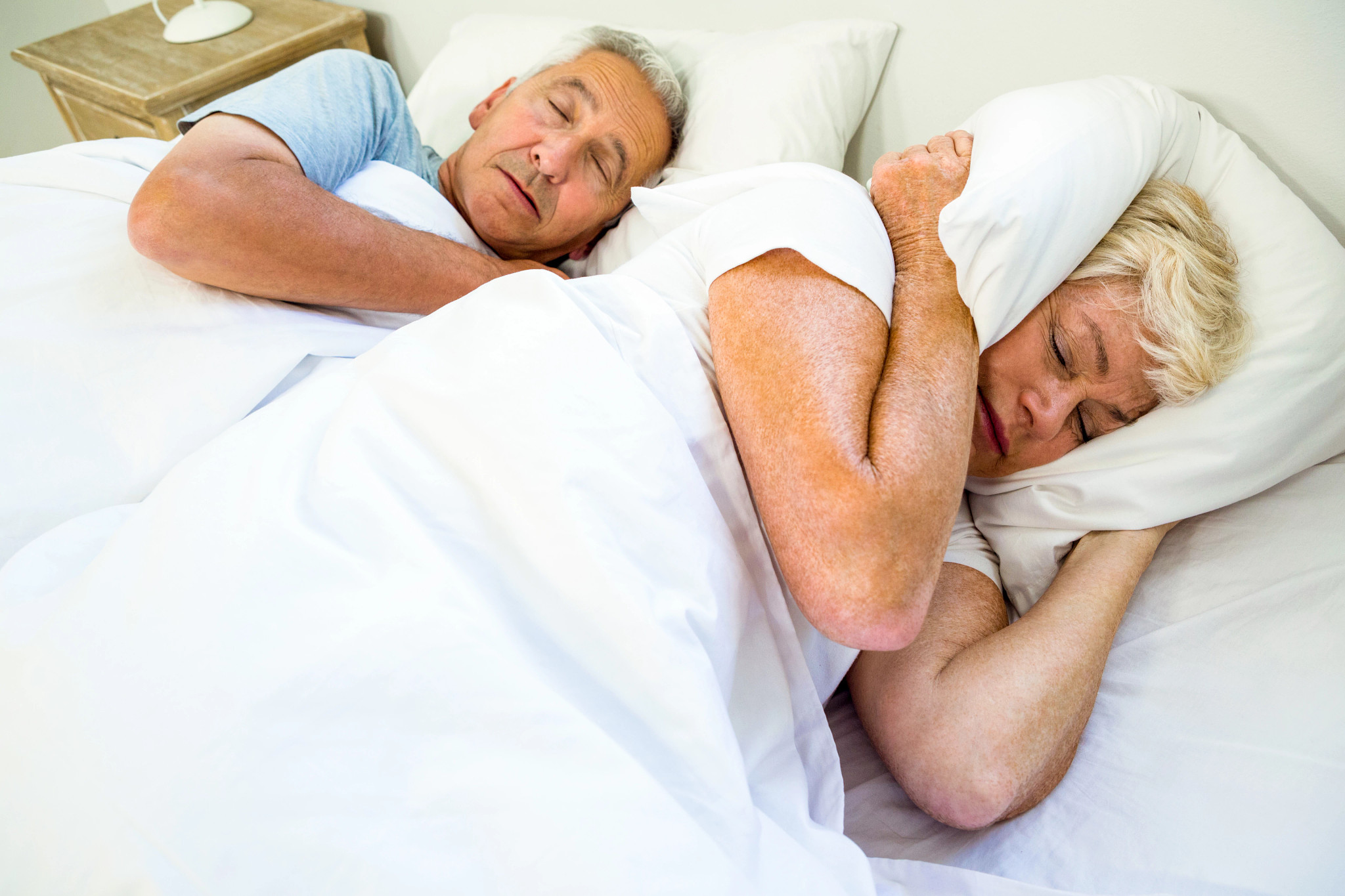 High angle view of woman sleeping by snoring man on bed at home