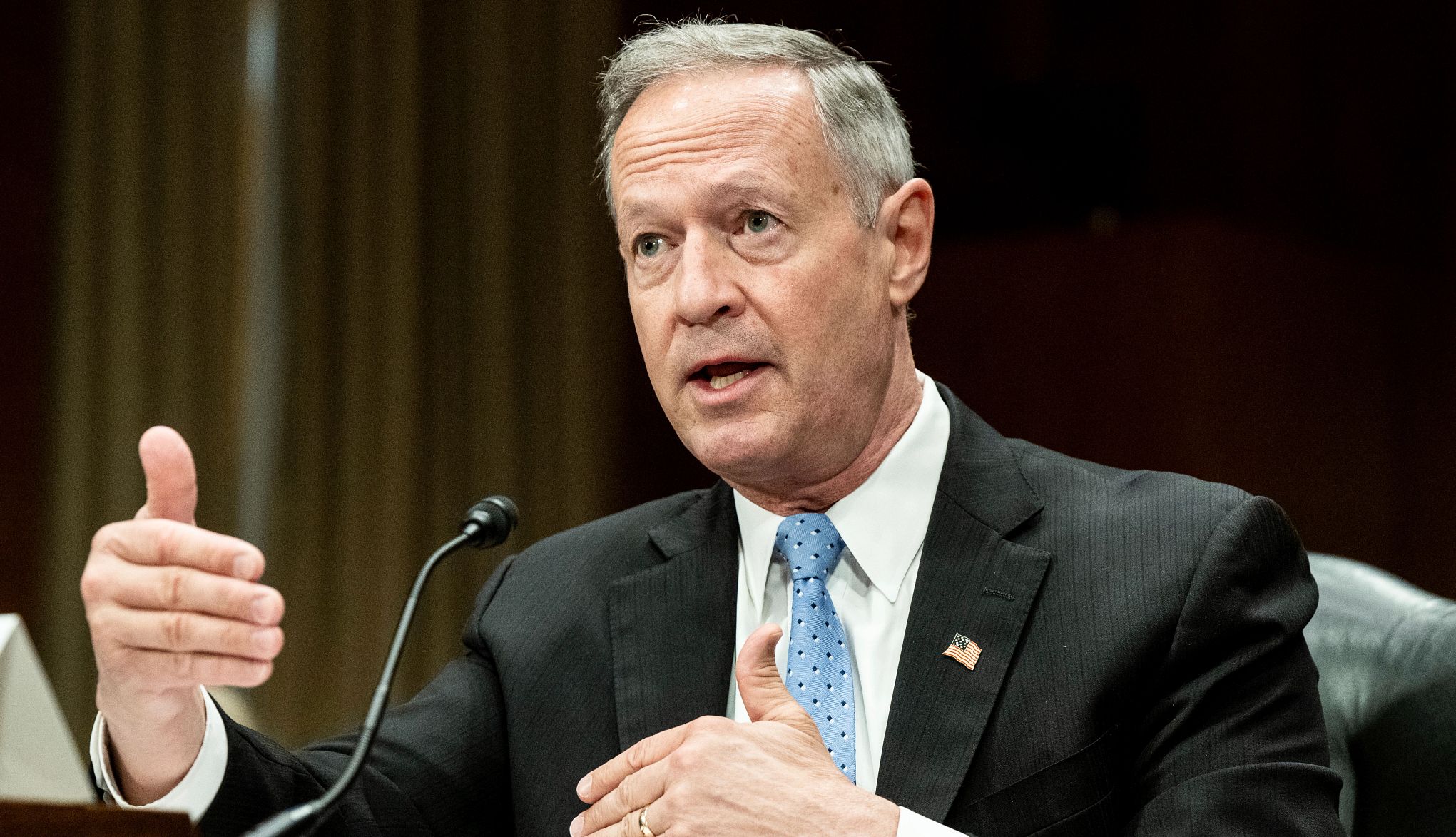 Social Security Administration Commissioner Martin O'Malley speaking at a desk into a microphone a man is sitting at a desk and speaking into a microphone