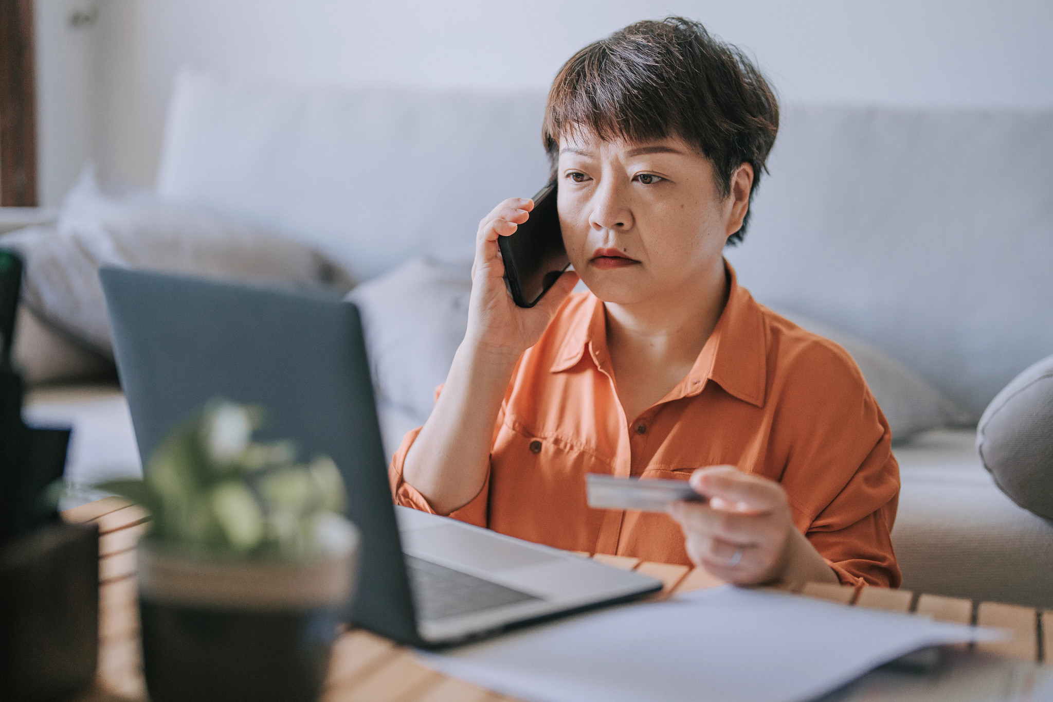 concerned asian mature woman communicate with bank through phone on fraud transaction at home