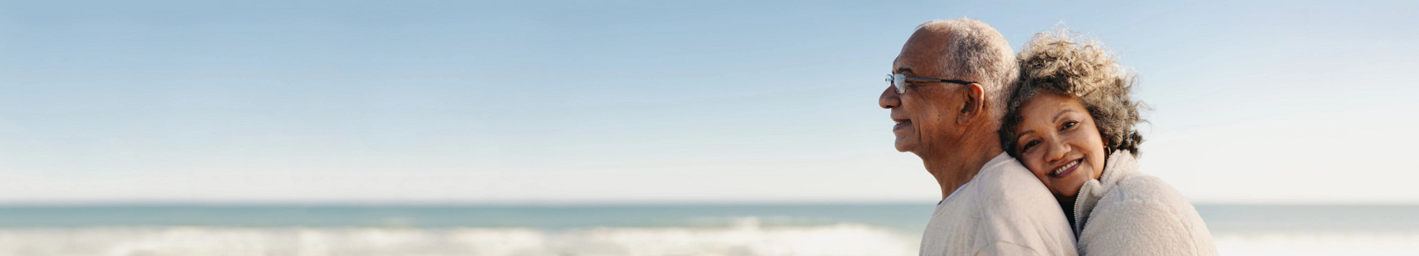 a woman hugging a man from behind as they stand on a beach