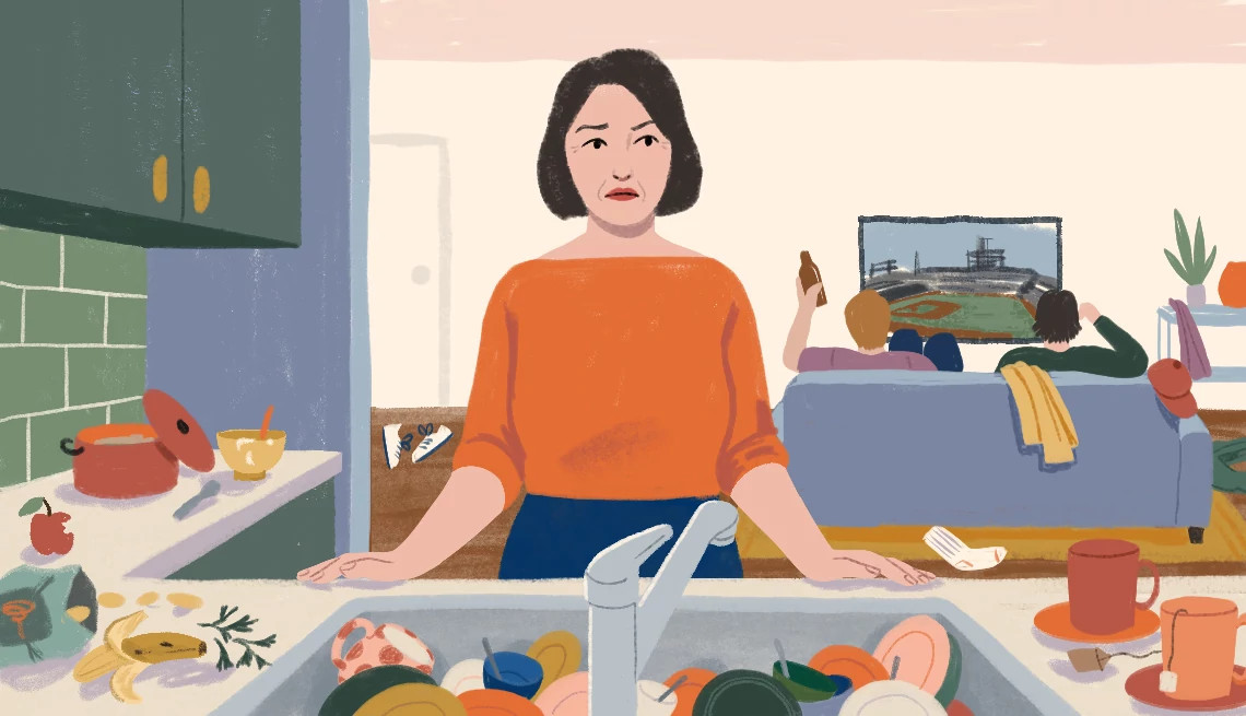 a woman stands at a sink full of dirty dishes while two men sit on the couch watching television behind her