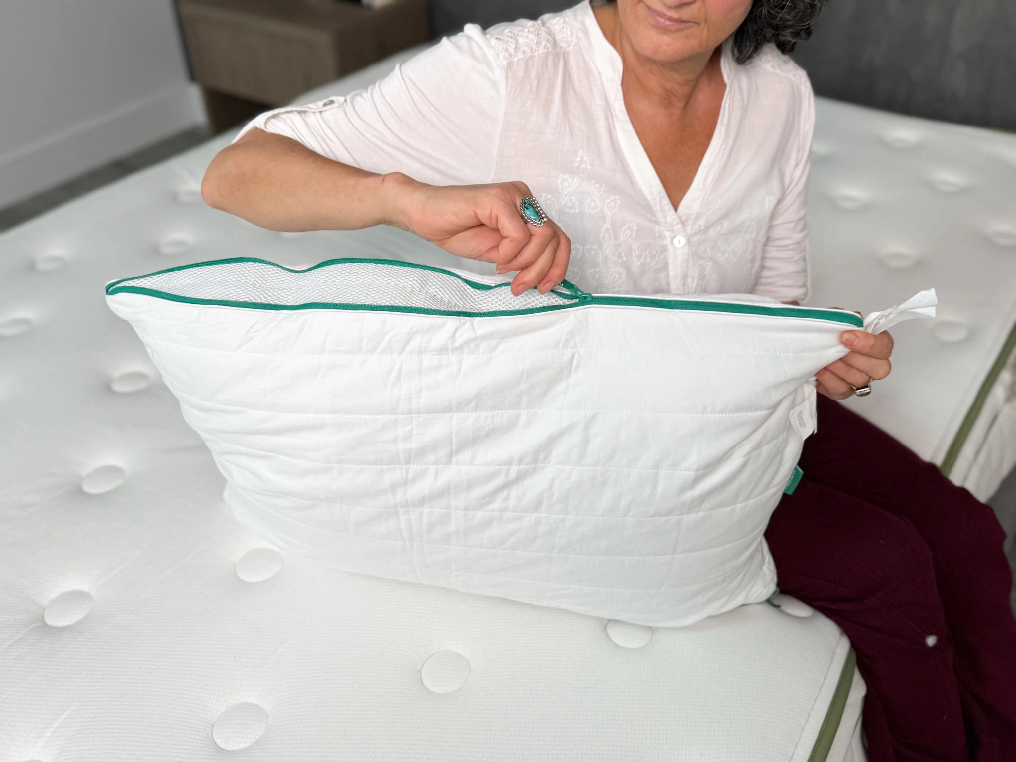  An older adult woman zipping up the side of the Brooklinen Marlow Pillow.