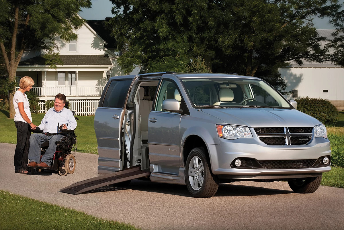 an older adult woman is shown in a photo helping a man in a wheelchair use a ramp to enter a wheelchair accessible van