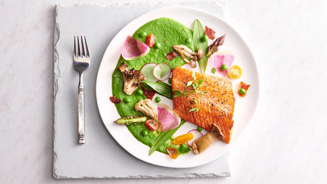 The Oceanaire Seafood Room white plate of food including salmon, pea puree, mushrooms, radish, other items, placed on stone placemat