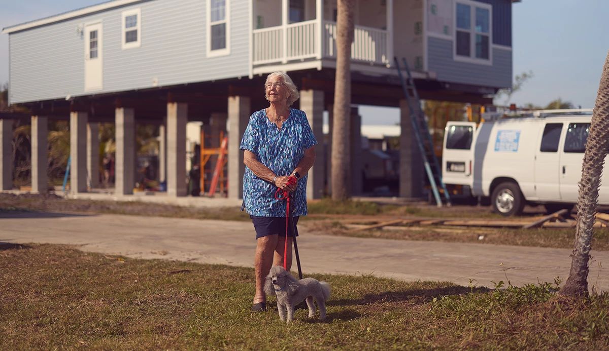 Women in blue blouse with small dog in front of a house on pillars