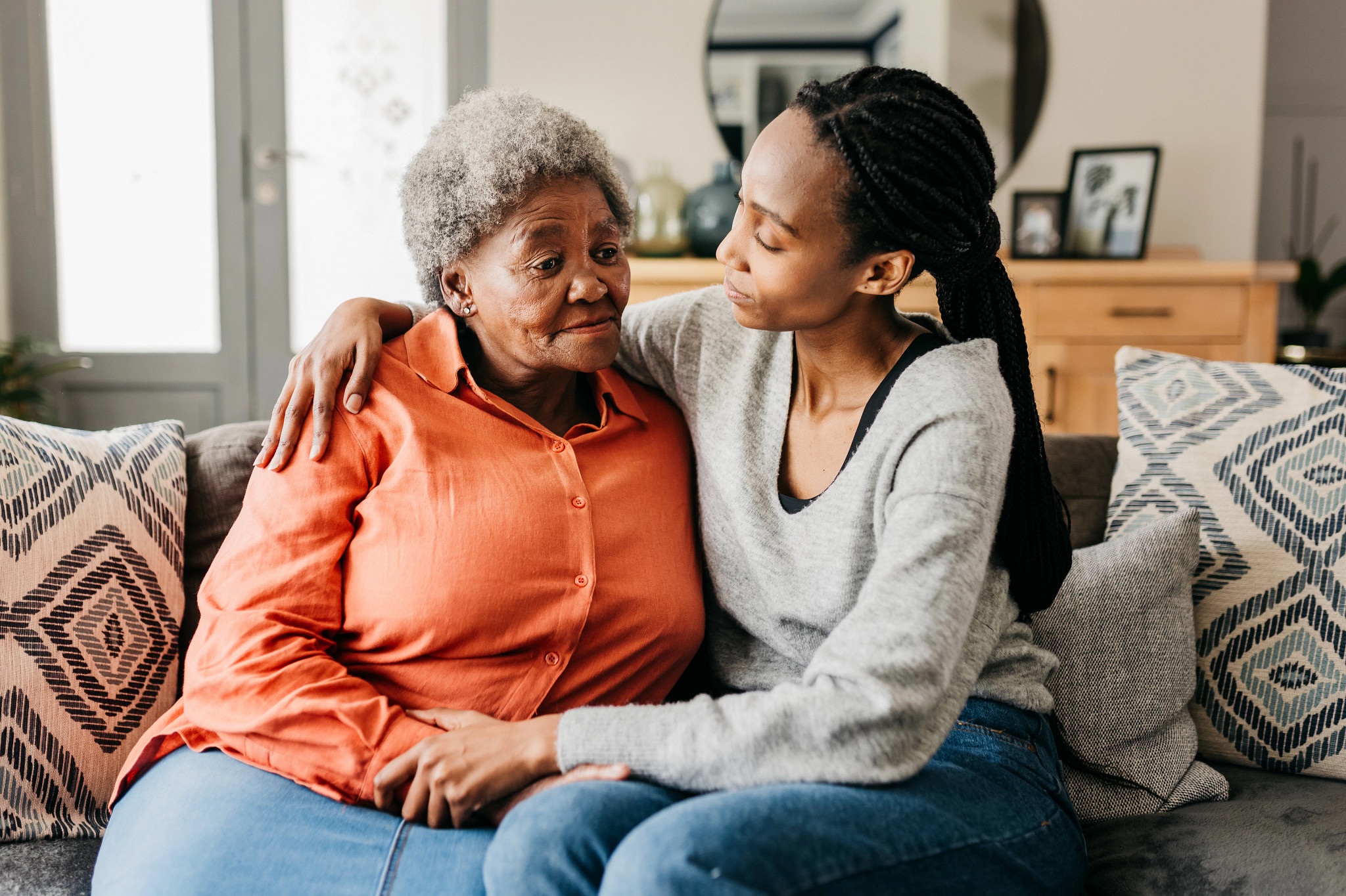 Young woman hugging sad mother comforting her on sofa at home