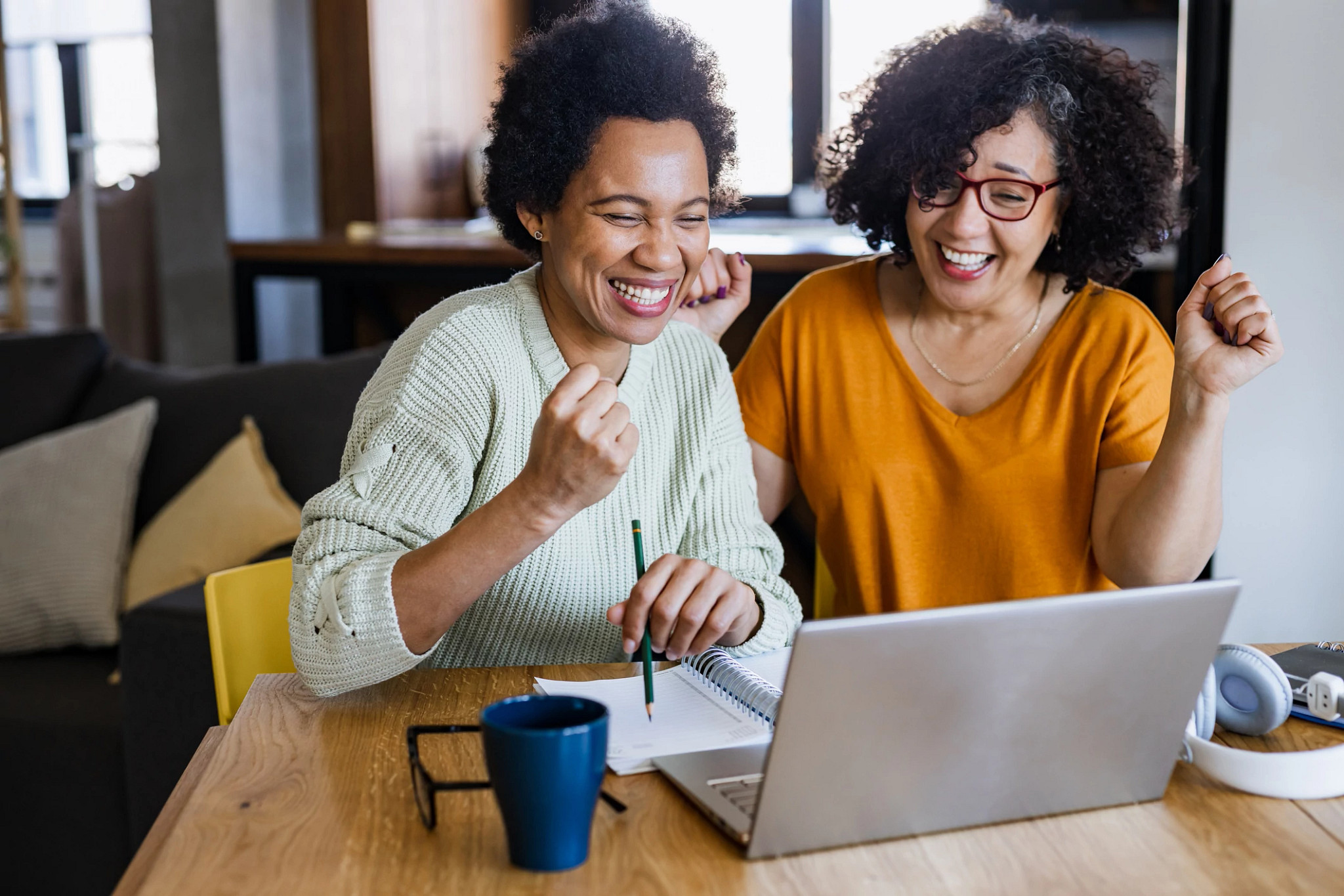 Two woman are using a laptop. They are feeling excited.