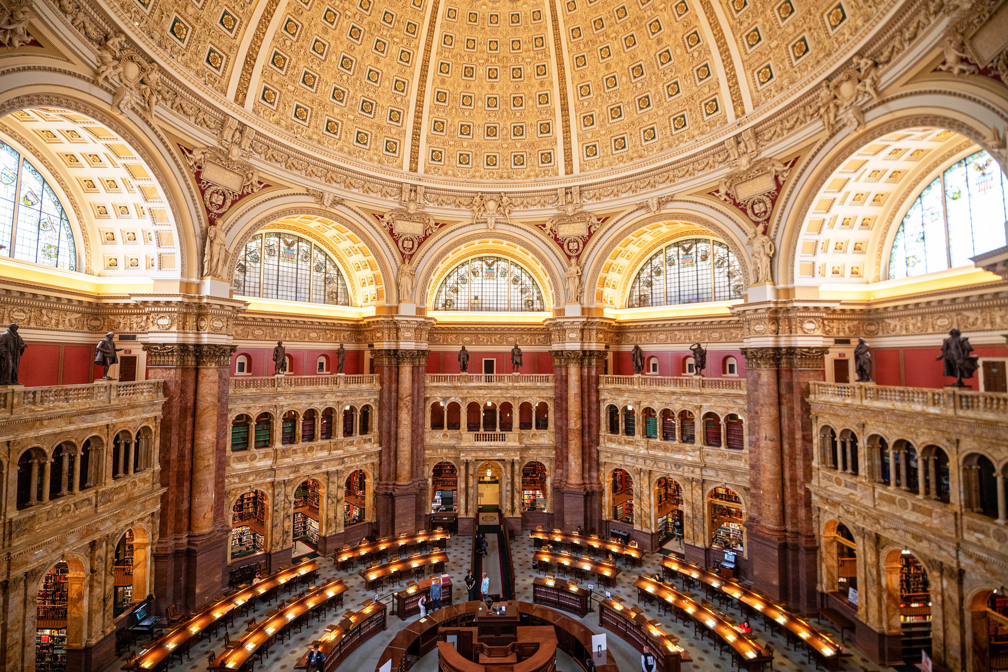 Large historic reading room with an ornate domed ceiling, arched galleries, library collections and illuminated study tables.