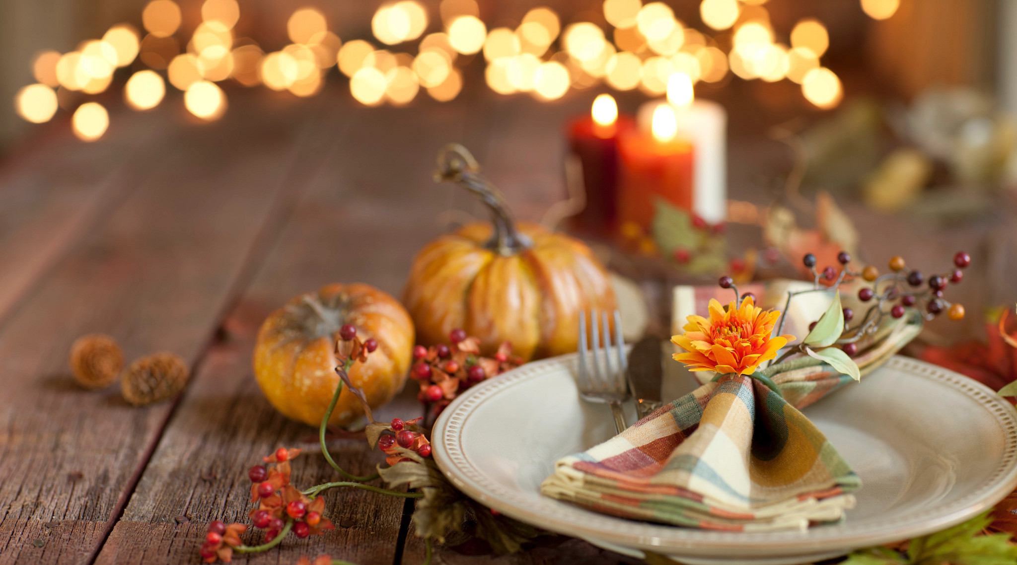 A group of people in their 30s and 40s crammed around a table covered in food at a Friendsgiving potluck dinner party in a loft apartment.