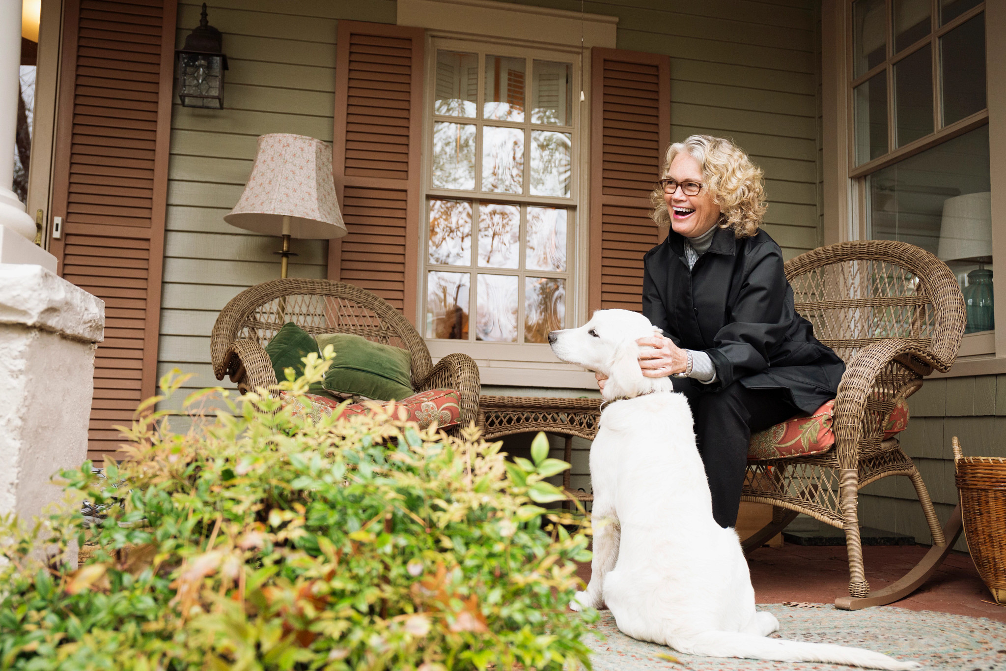 a woman petting a dog and laughing while sitting in a chair on a porch