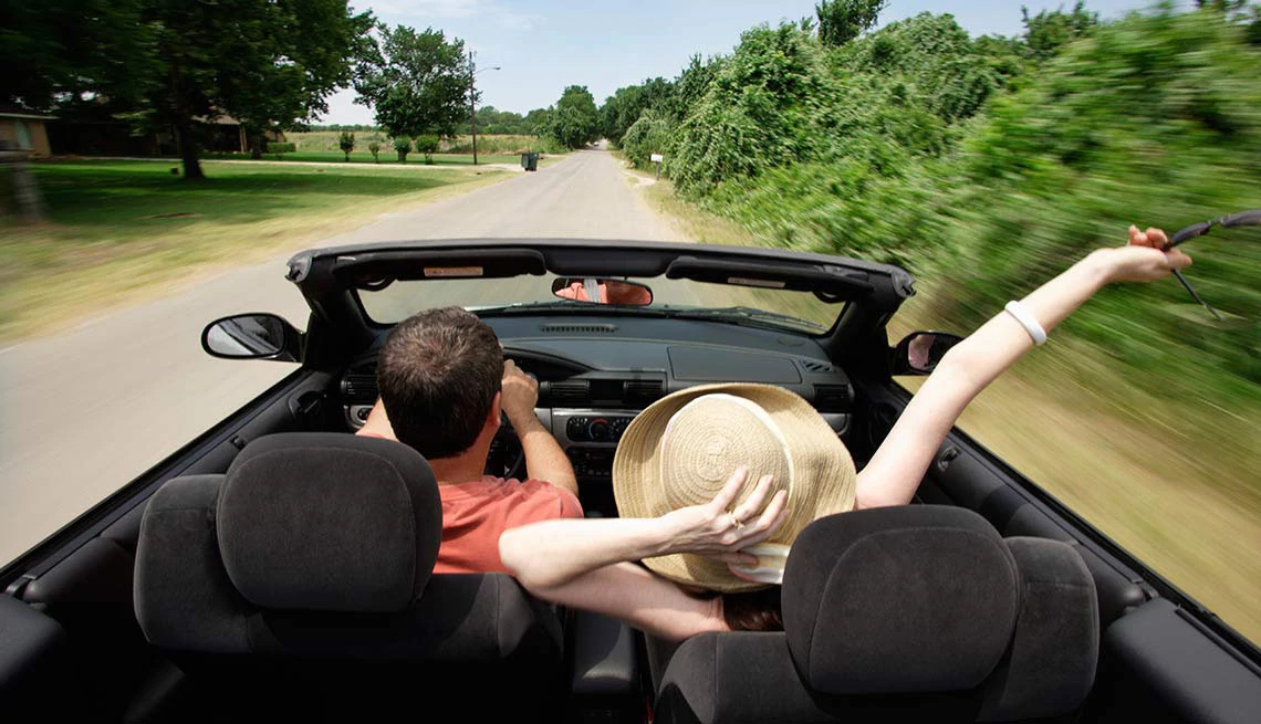 Payless® Car Rental man and woman in top down convertible car driving on a country road, sunny day
