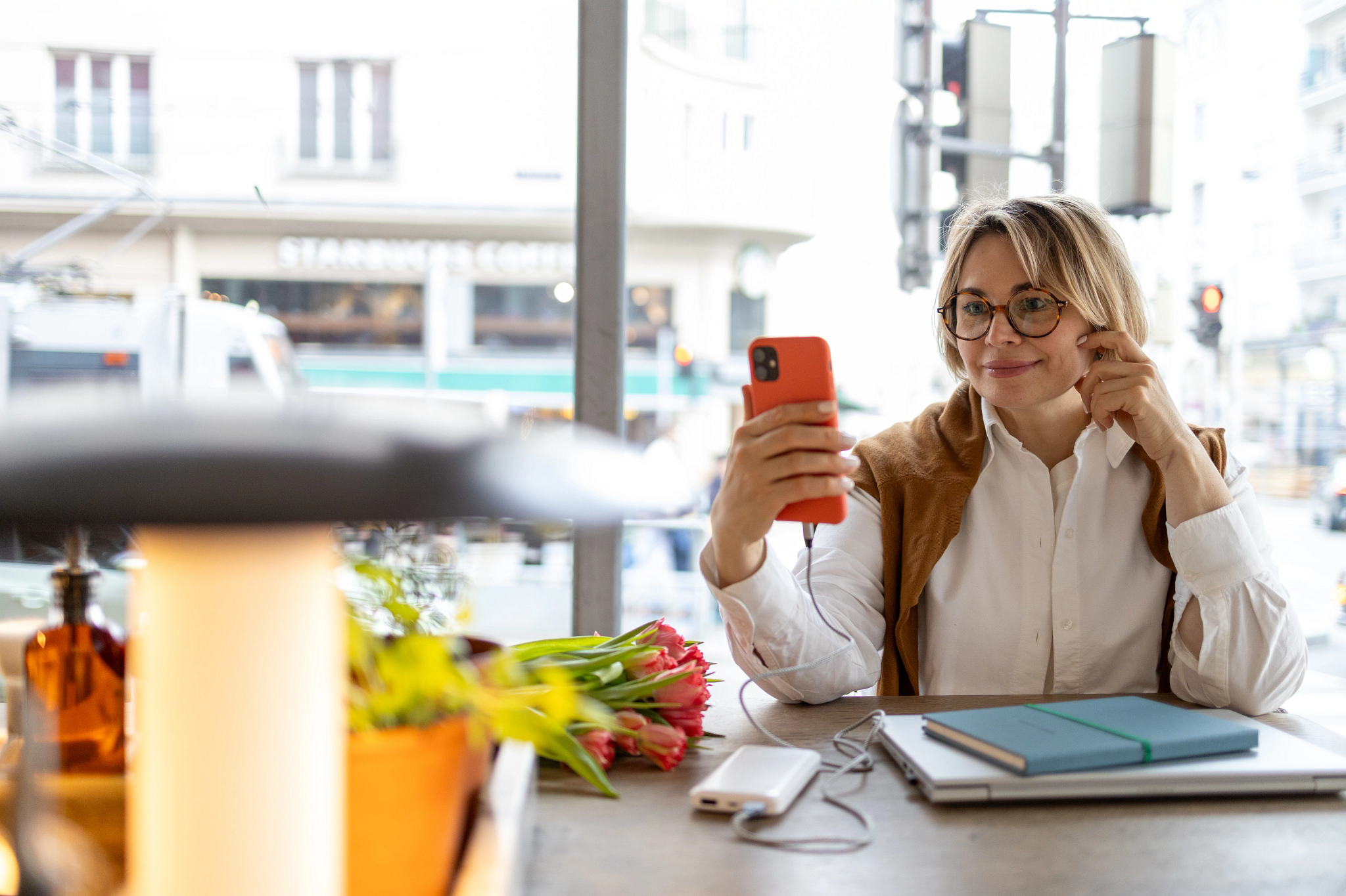 a woman is looking at her smartphone while sitting at a table with her laptop