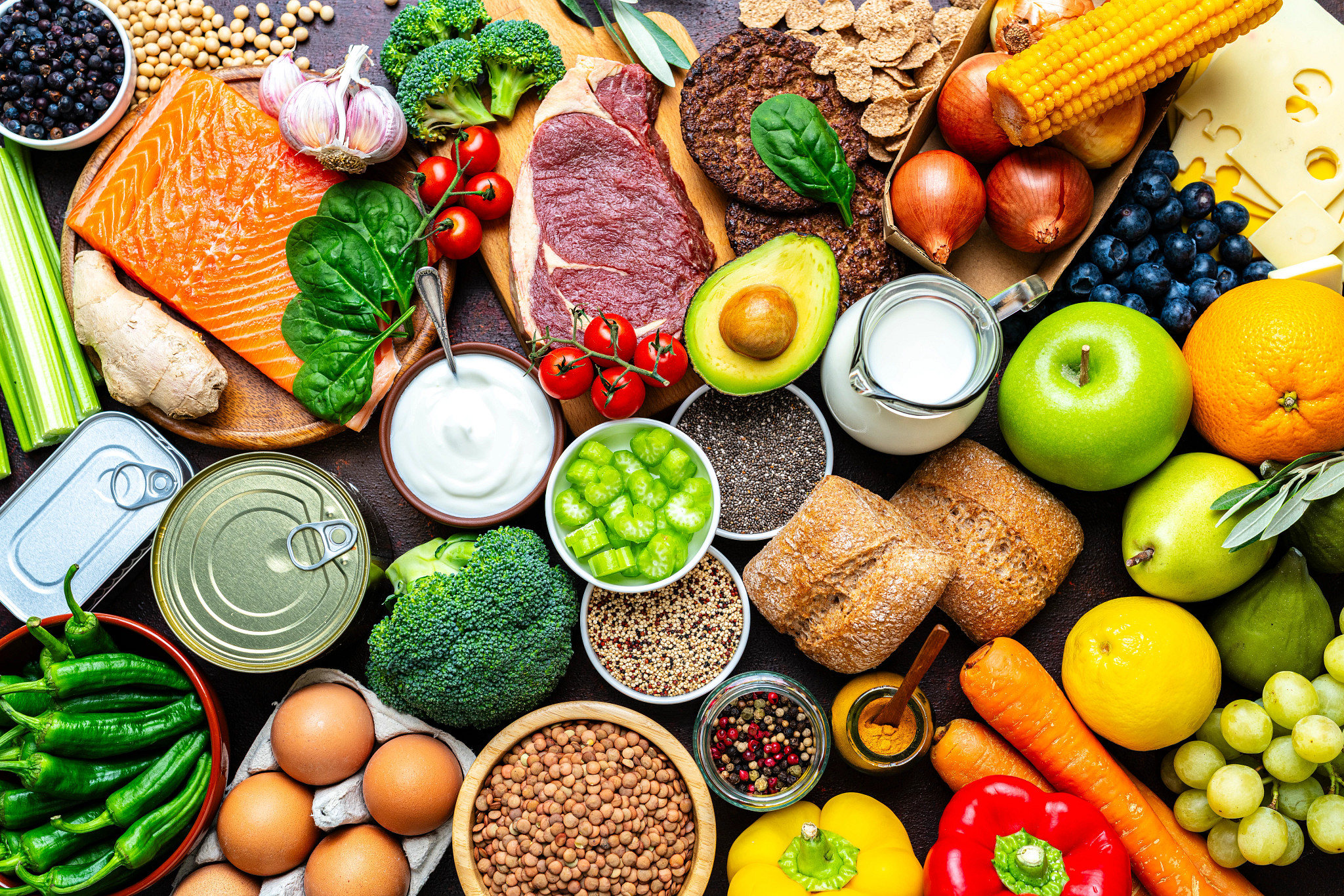 a top down view of an abundance of healthy foods, including fruits, vegetables, bread, raw grains, raw proteins and some canned proteins