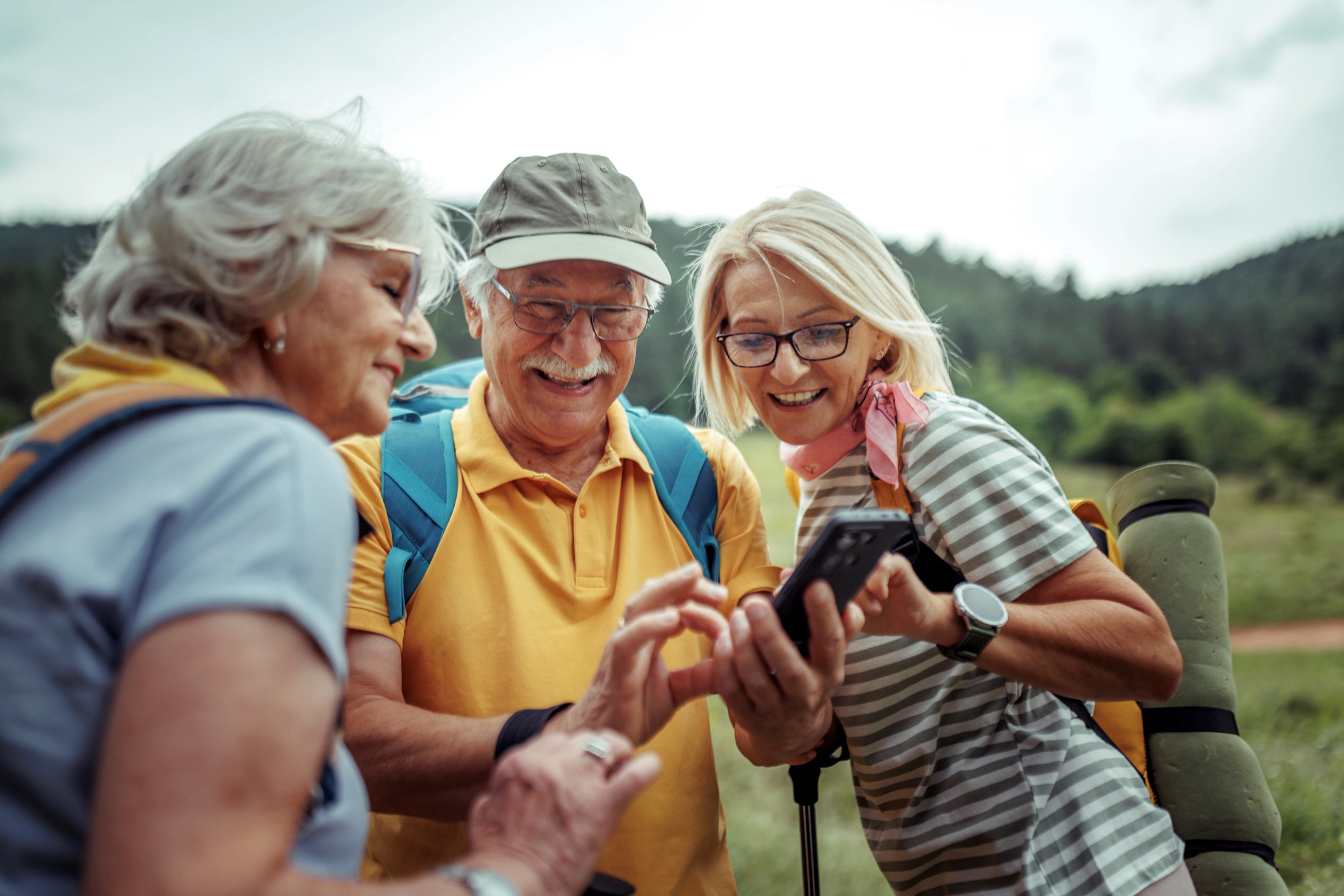 Group of senior hikers using smart phone while hiking together in forest