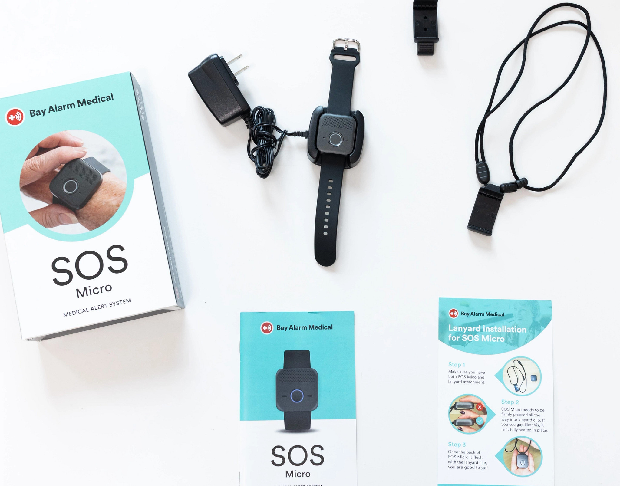 The Bay Alarm Medical SOS Micro medical alert system on a table with the charger, manual and packaging around it