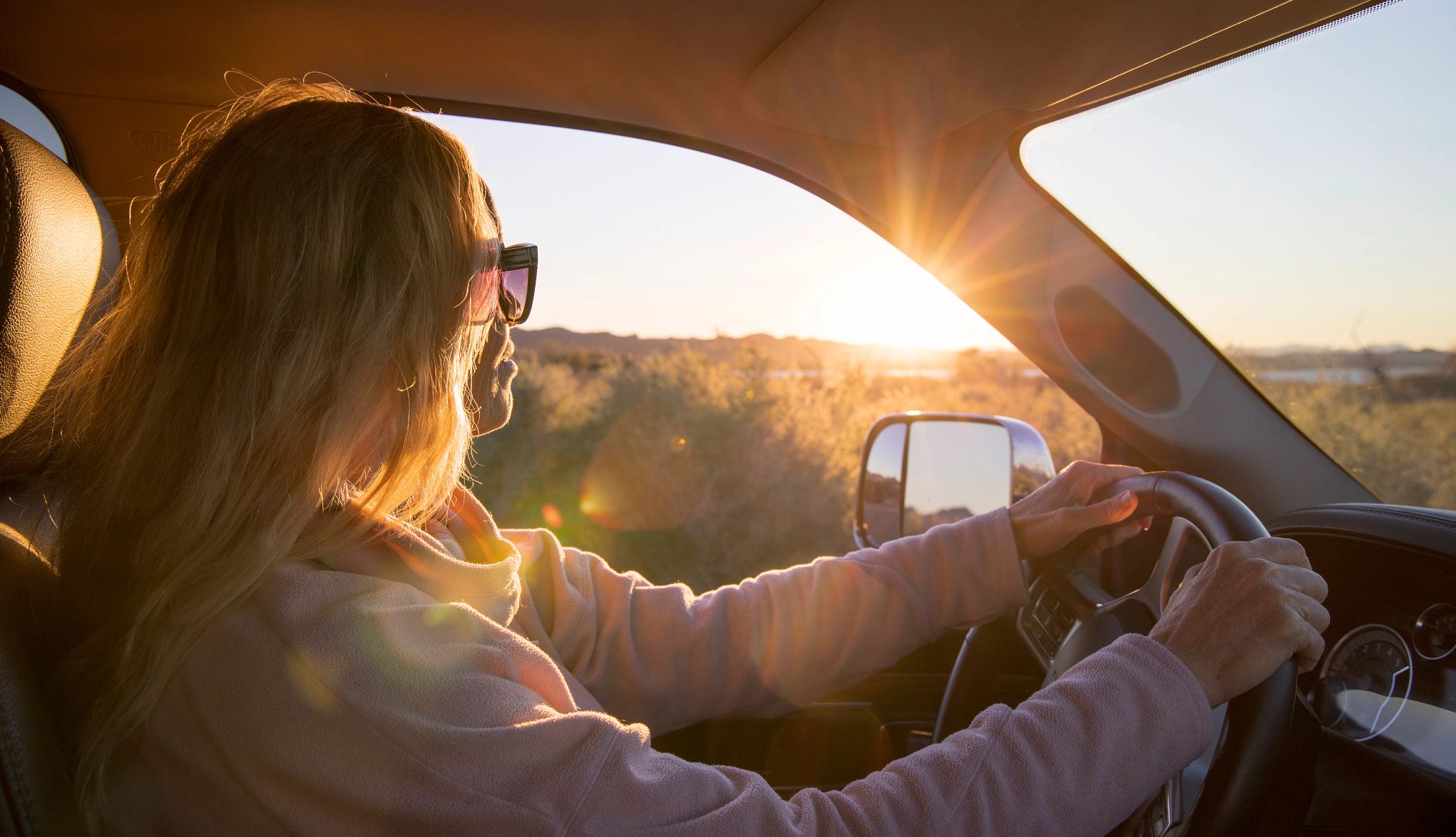 Una mujer conduce un auto al amanecer.