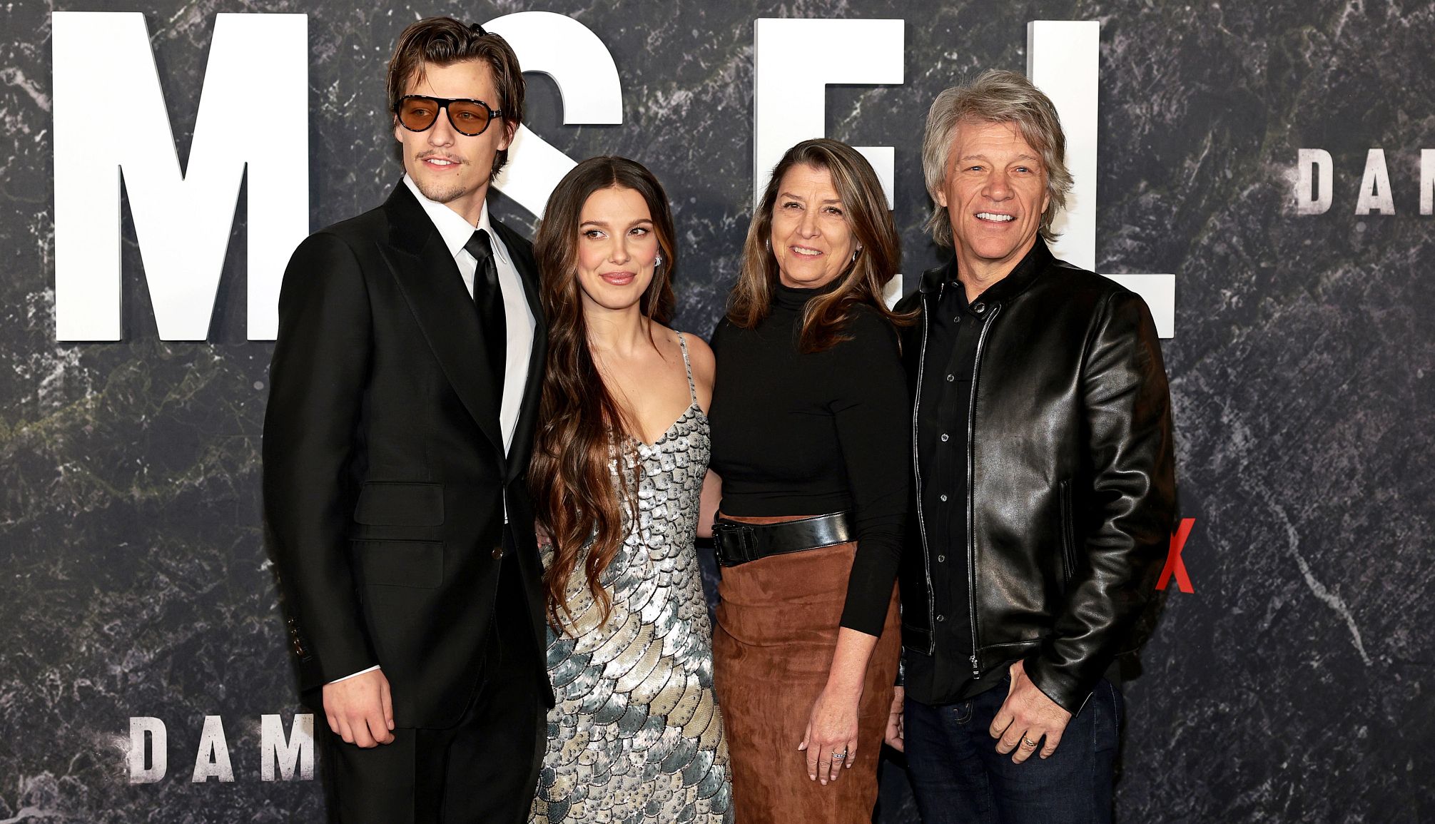 Jon Bon Jov is Rocking His New Granddad Role Jake Bongiovi, Millie Bobby Brown, Dorothea Hurley, and Jon Bon Jovi smiling for a red carpet photo