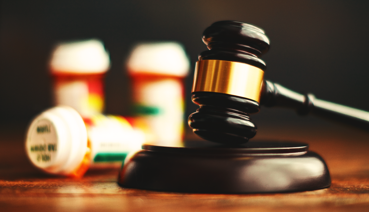 A close-up of a legal gavel with blurred prescription medication bottles in the background.