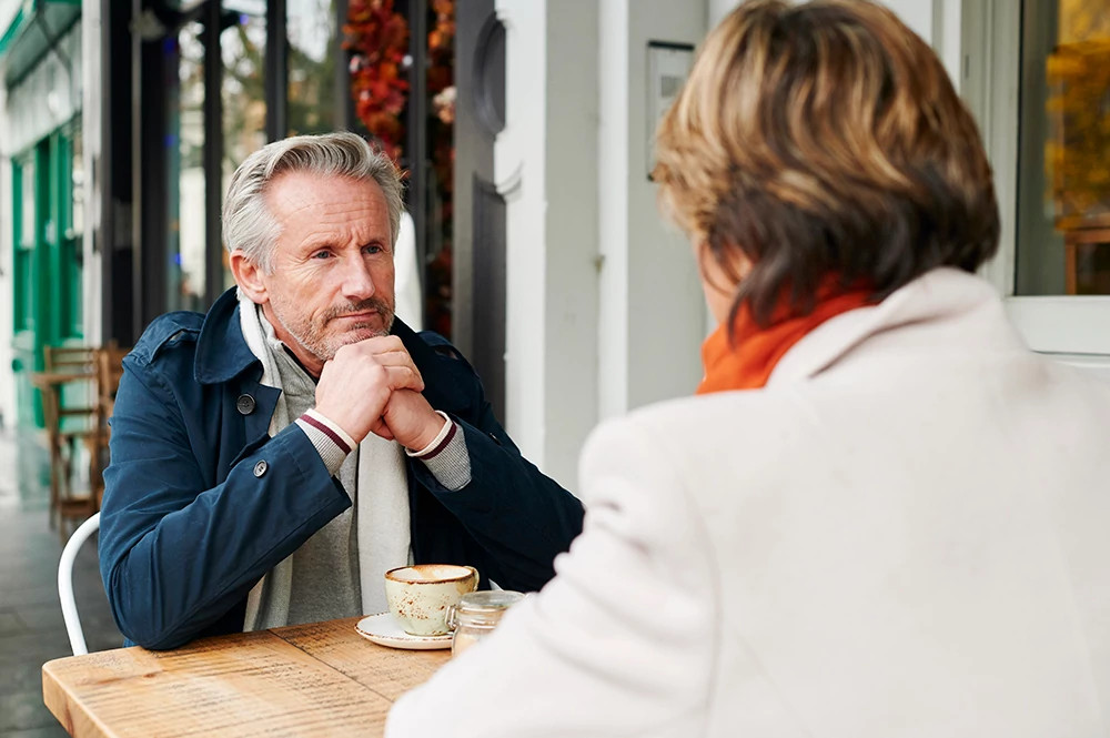 man looking at a woman he's sitting with outside of a cafe