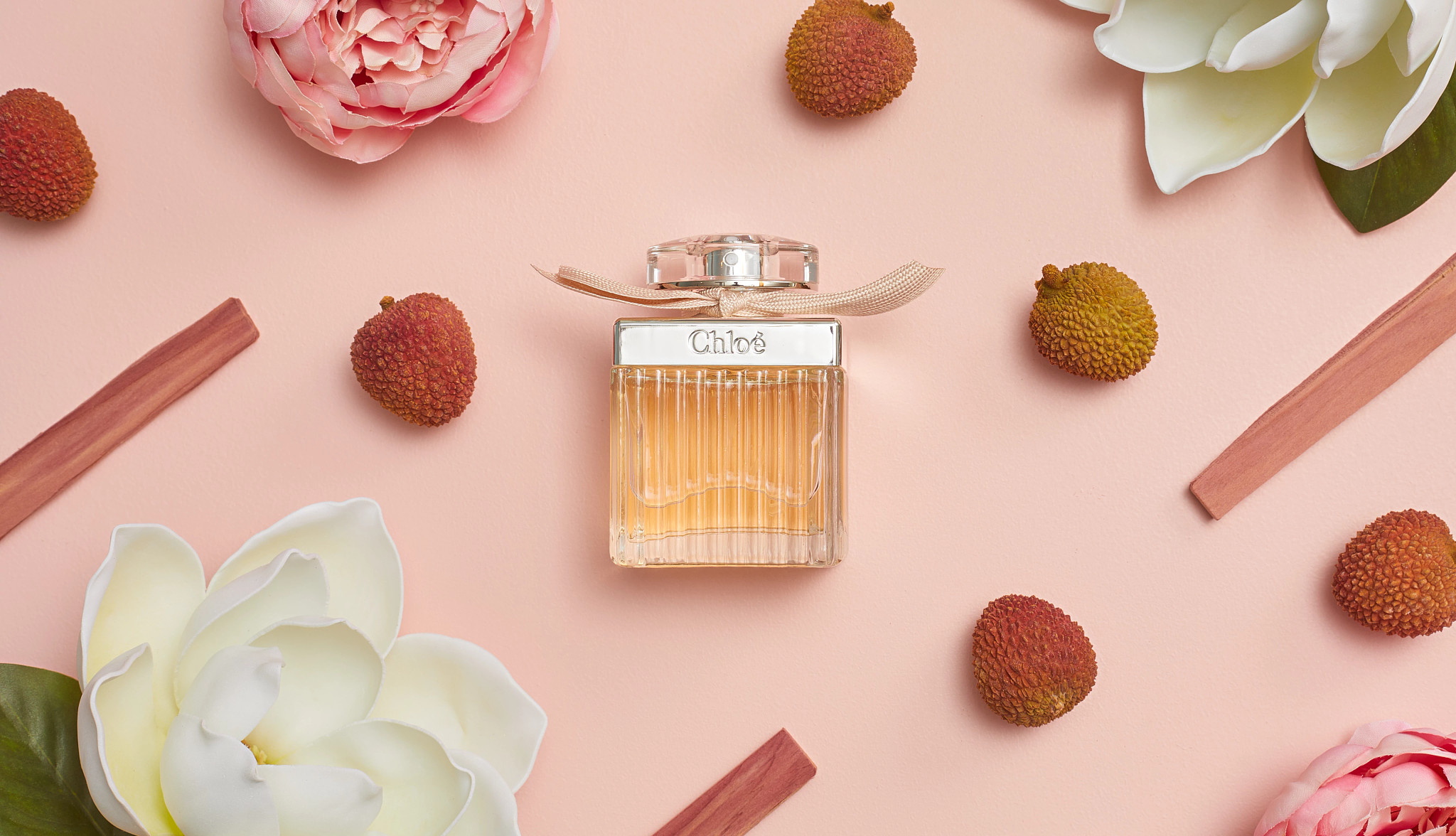 Bottle of Chloé Eau de Parfum surrounded by pink peonies, lychee, magnolia flowers, and cedarwood 